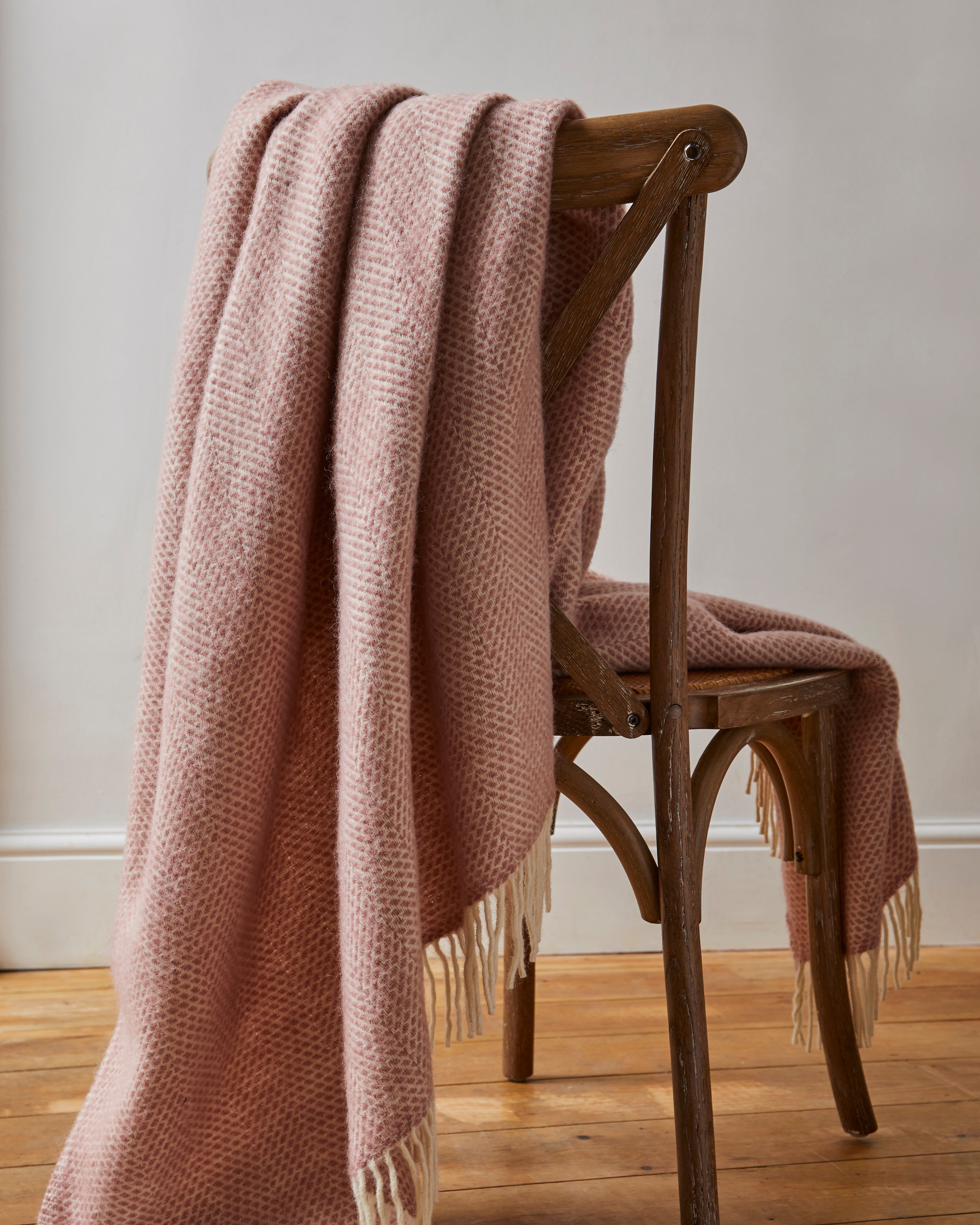 Pink wool blanket draped over a wooden chair against a plain wall.