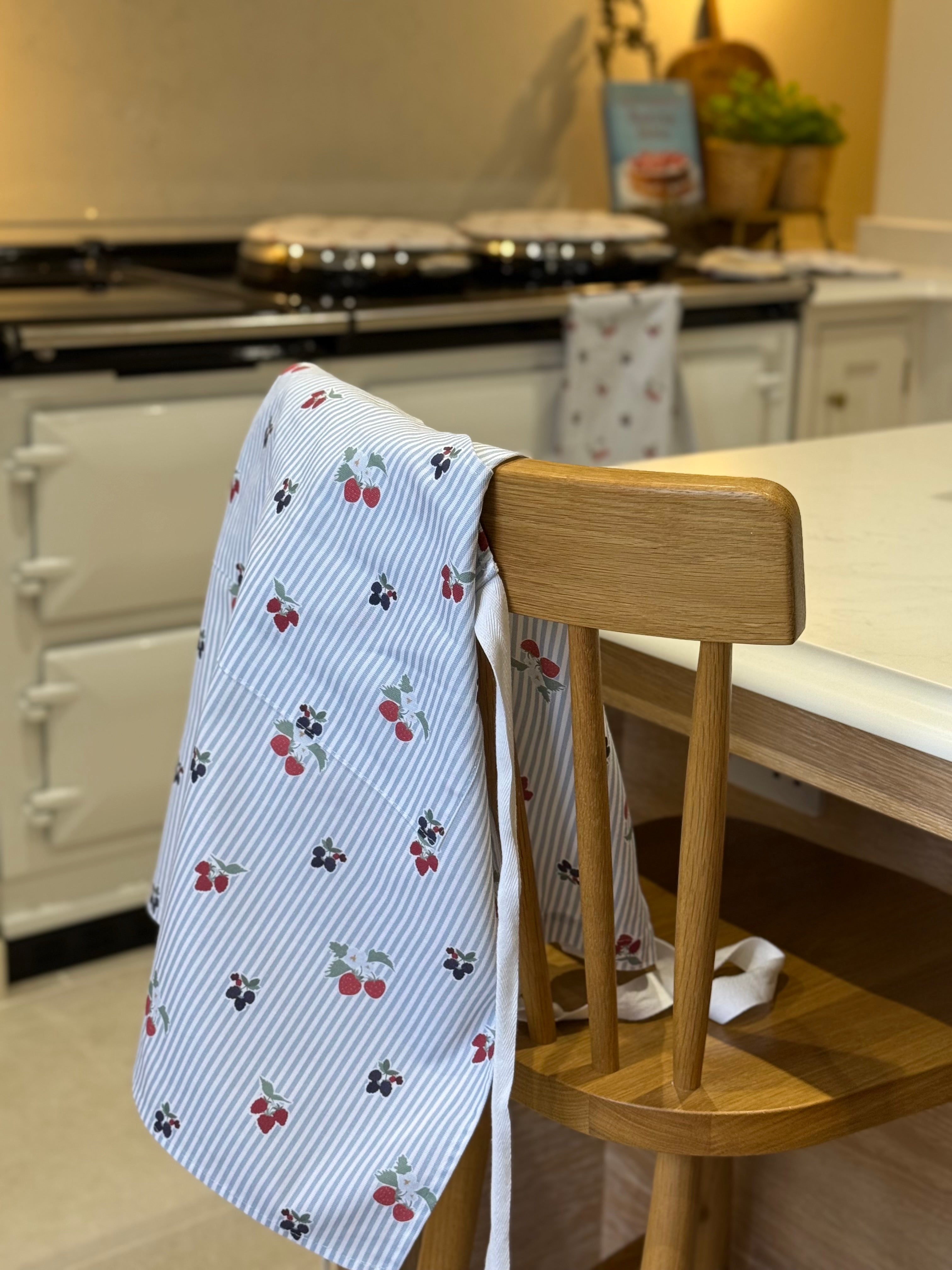 Kitchen scene with a wooden chair and berry-patterned towel draped over it, Aga range cooker in the background.