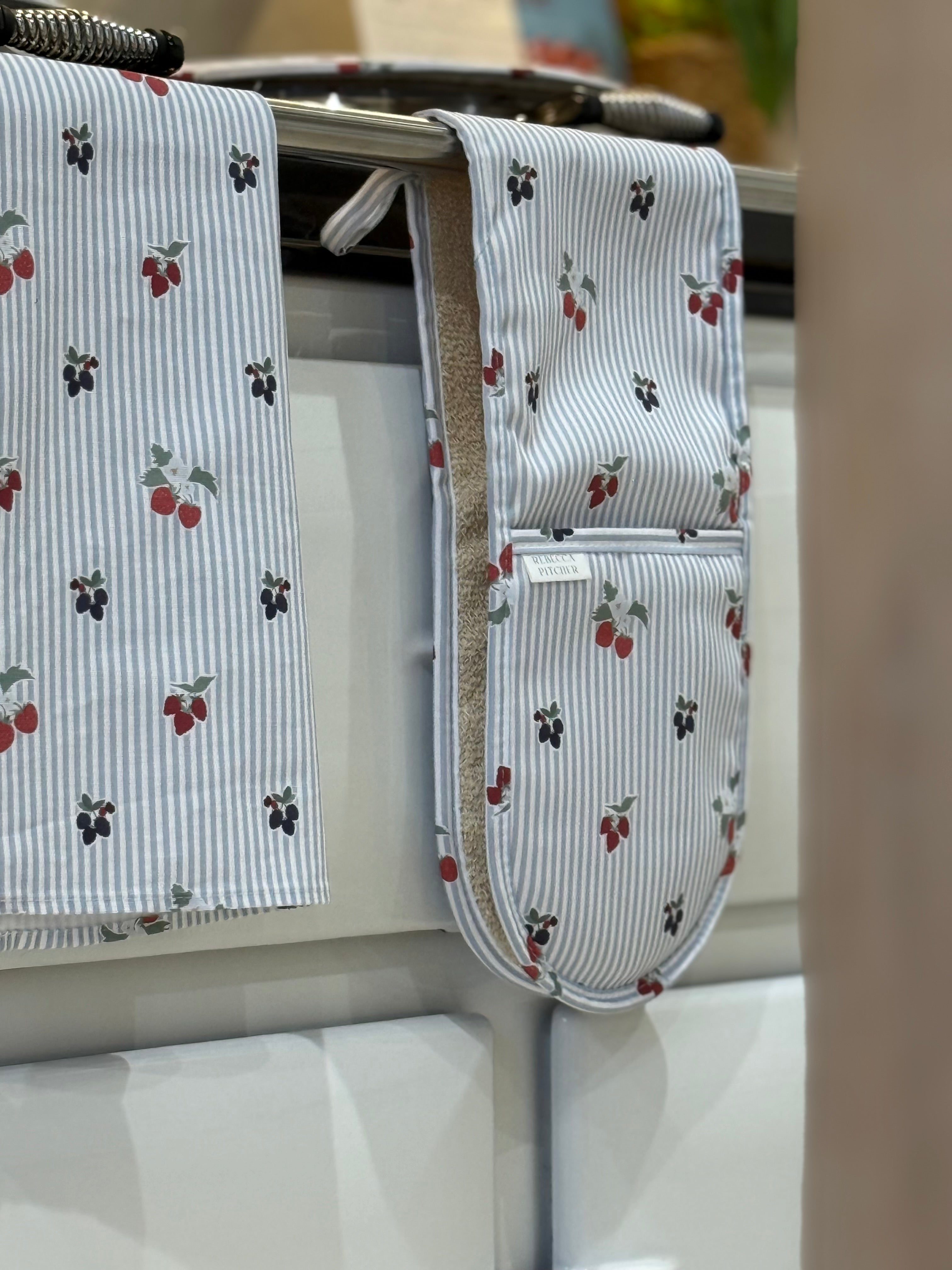 Set of kitchen towels and double ovengloves with berry pattern hanging on a range cooker.