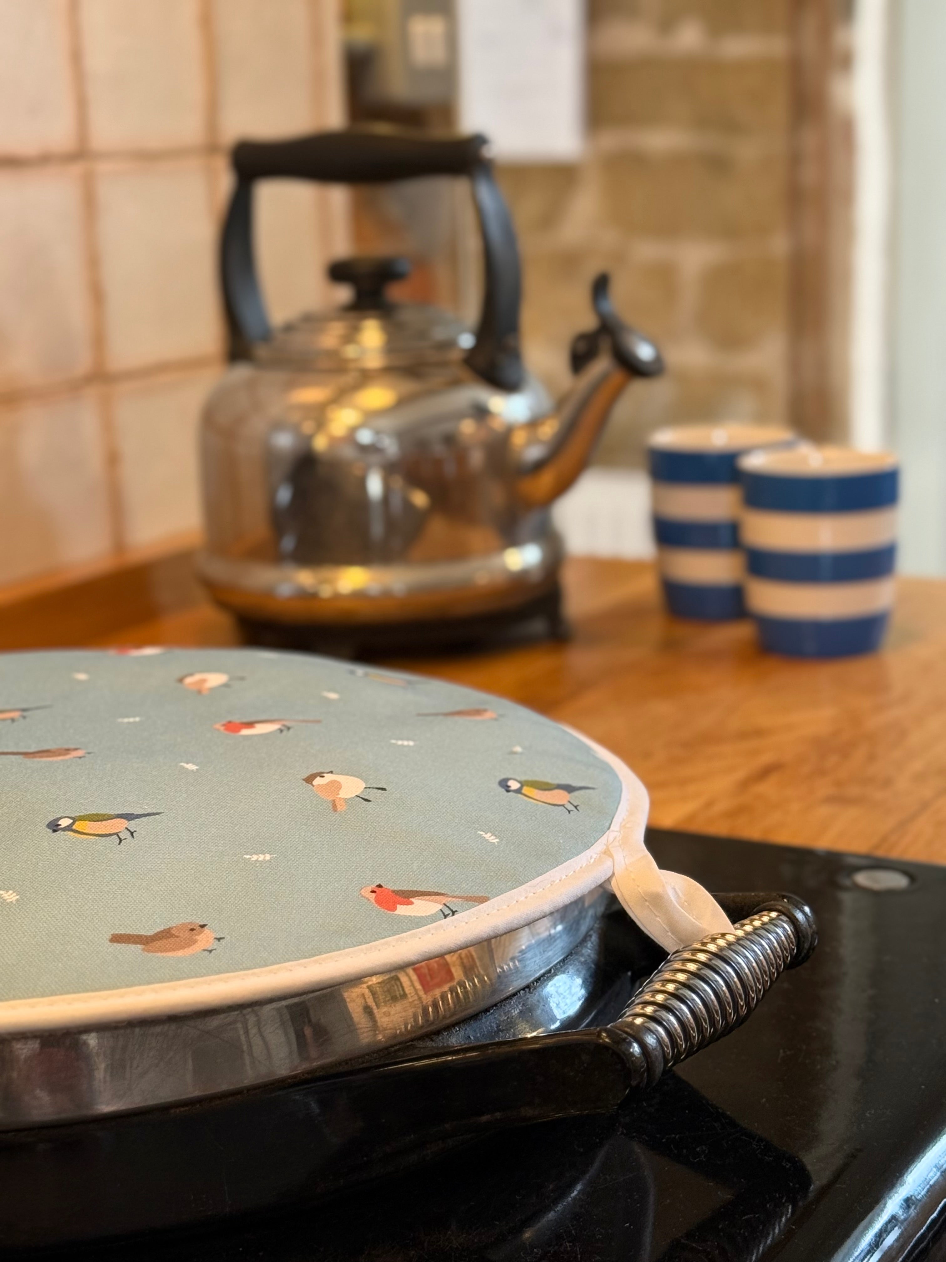 Hob cover with garden bird pattern on a stove, with a kettle and cups in the background.