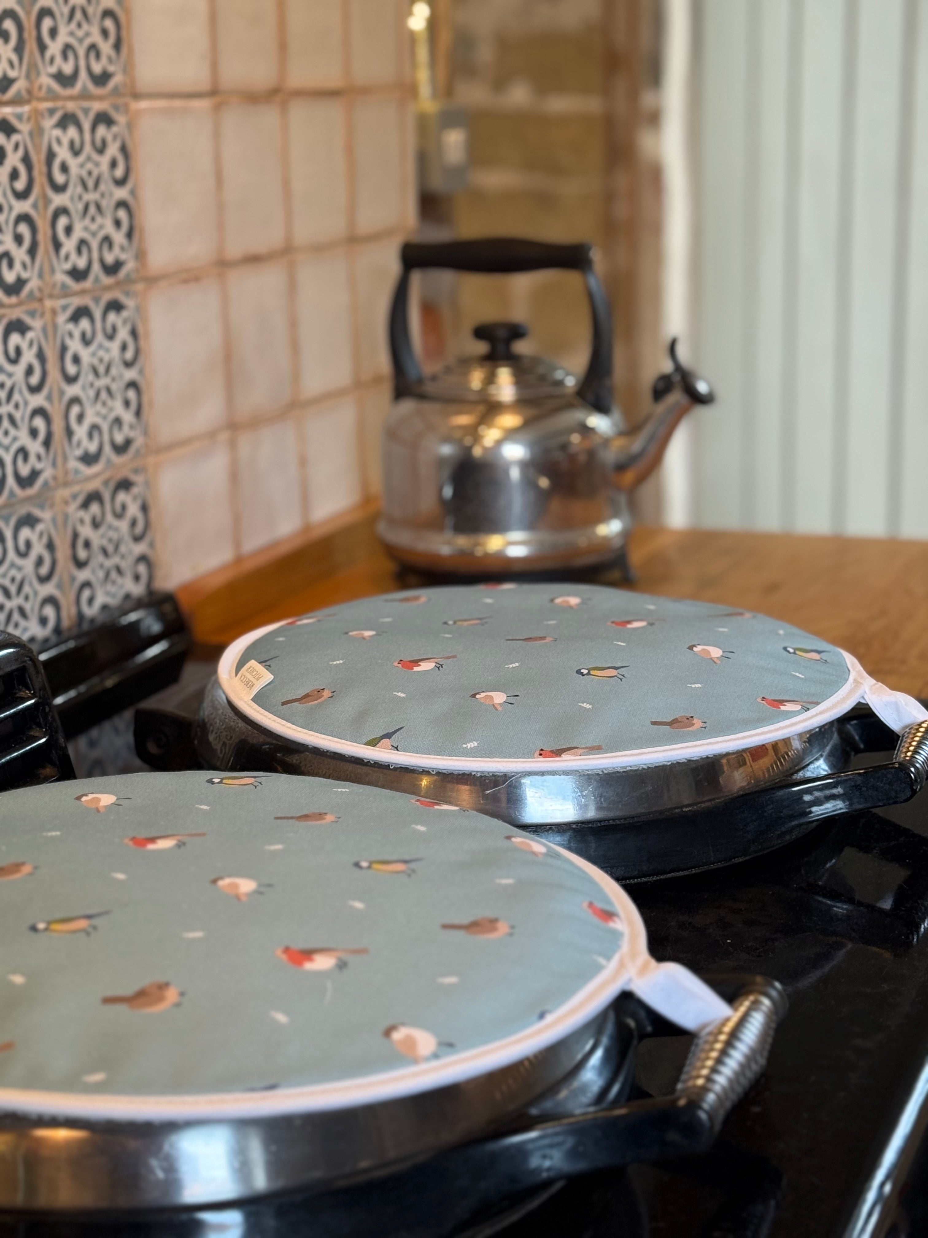 Two round bird patterned hob covers on a stove, with a silver kettle in the background.