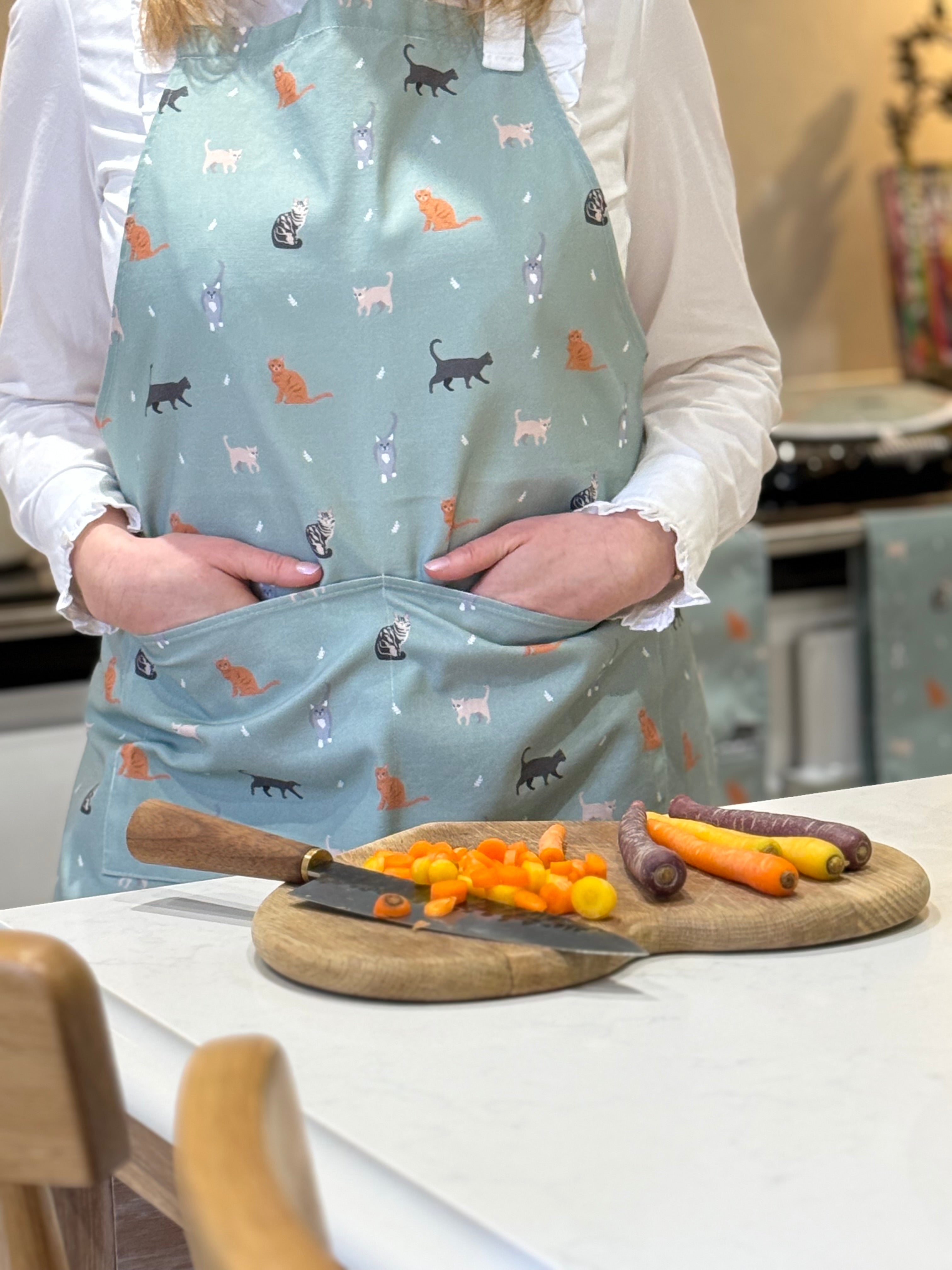 Person wearing a light green apron with cat patterns in a kitchen setting.