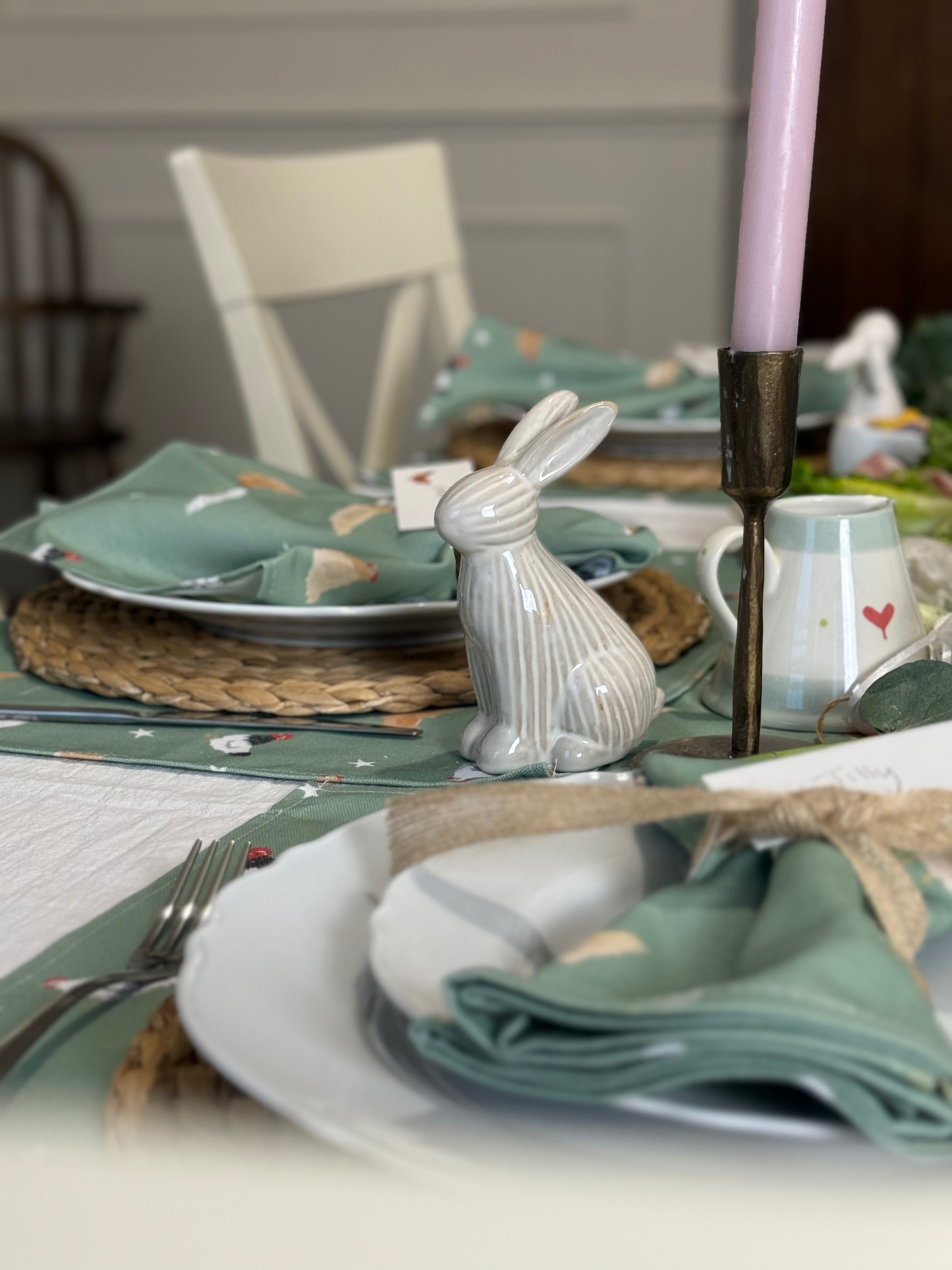 Easter table setting with bunny figurine, green chicken pattern napkins, and candles.
