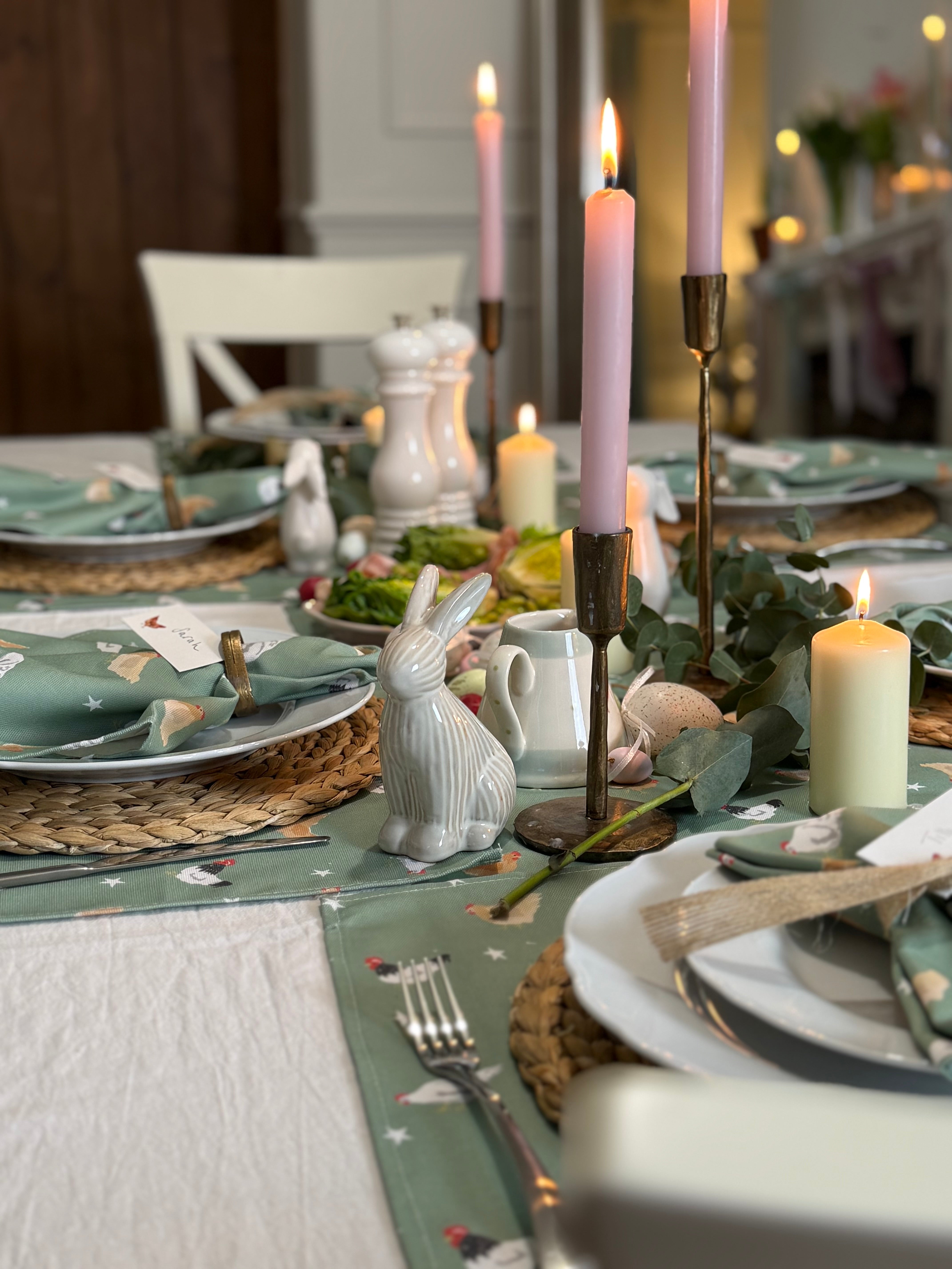 Easter-themed table setting with bunny figurines, candles, and green chicken design placemats.
