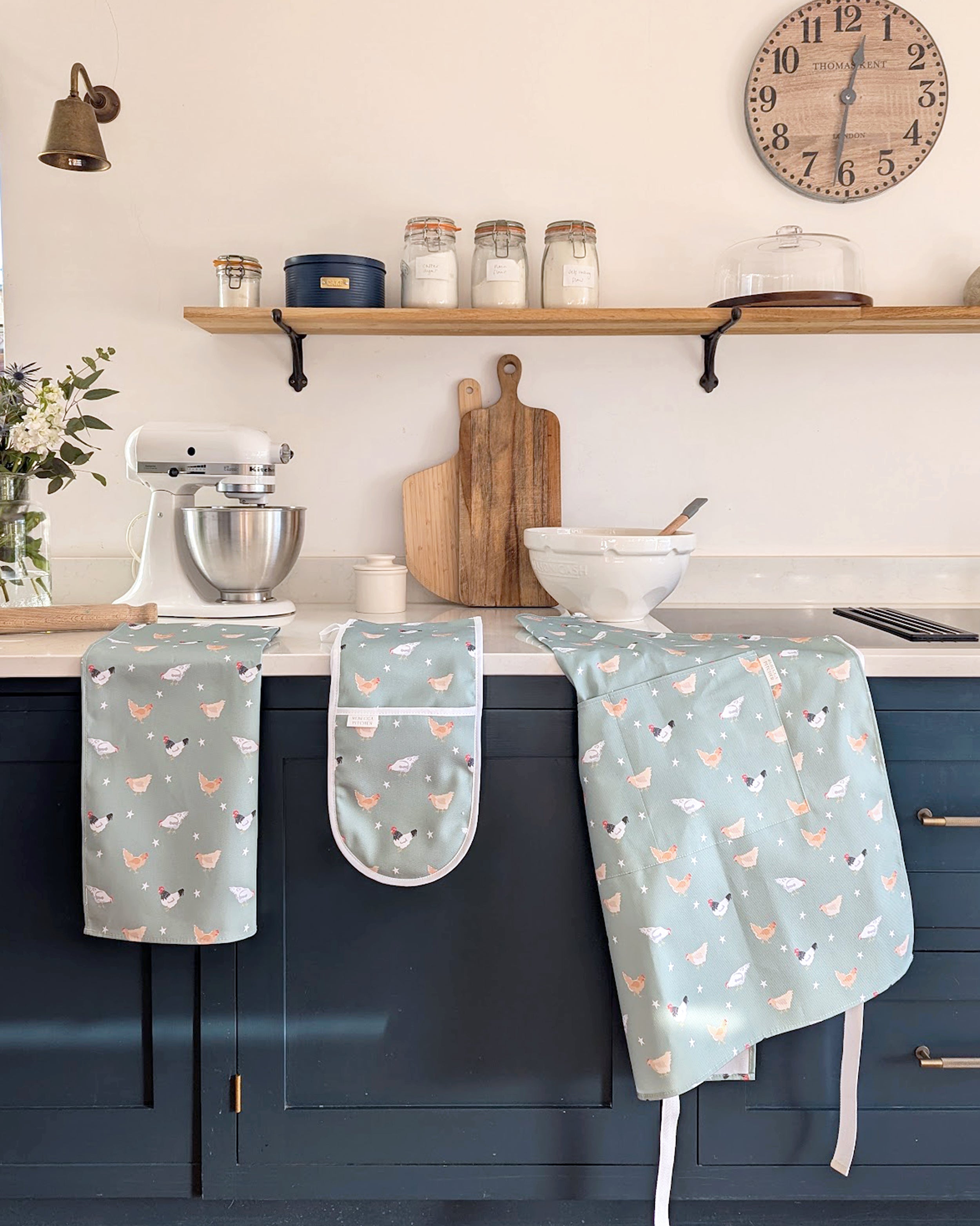 Kitchen counter with green chicken pattern aprons, oven mitt, and kitchen tools on a neutral background