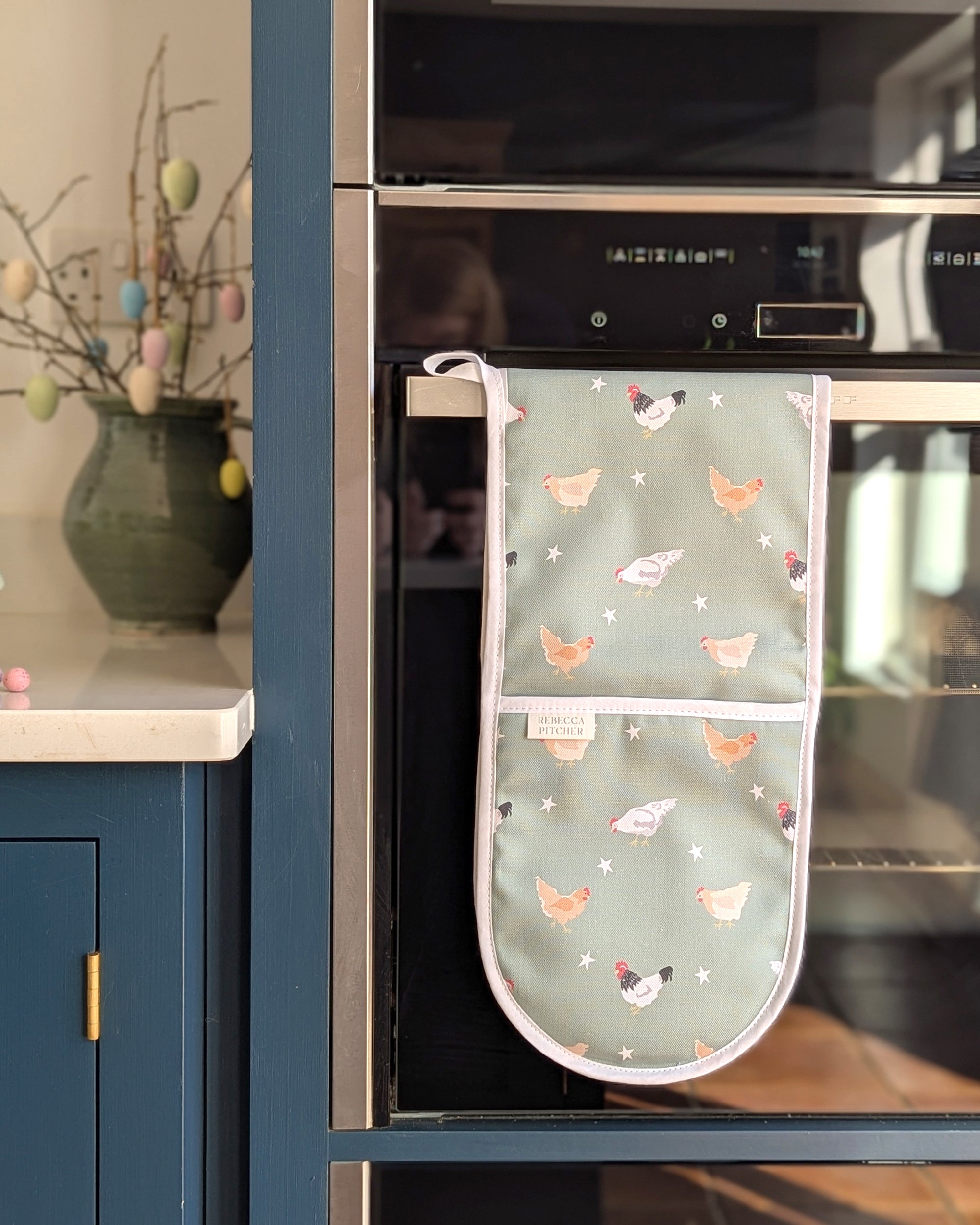 Oven mitt with chicken pattern hanging on a kitchen oven