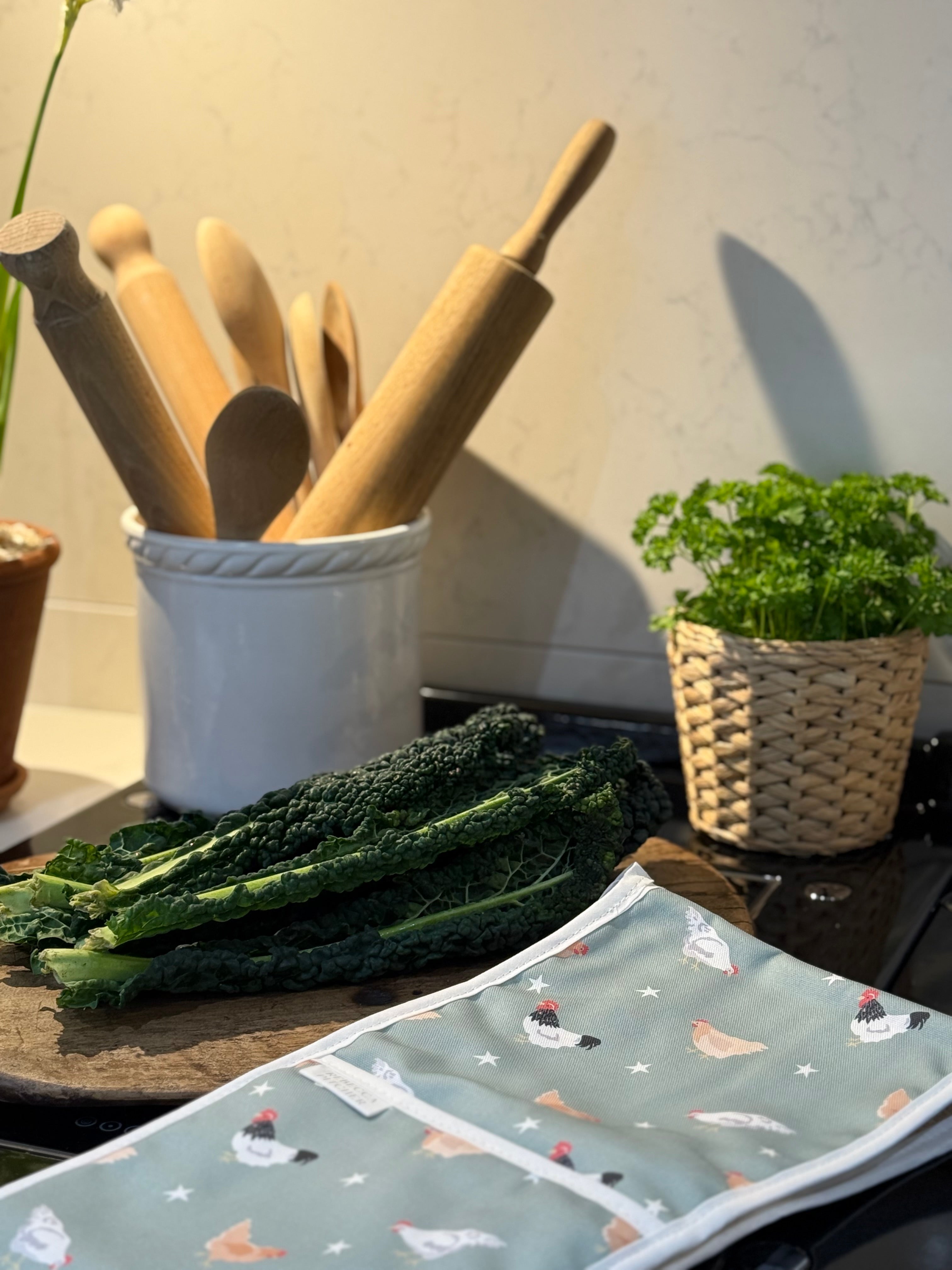 Chicken design oven glove on a kitchen worktop with utensil pot and leafy food