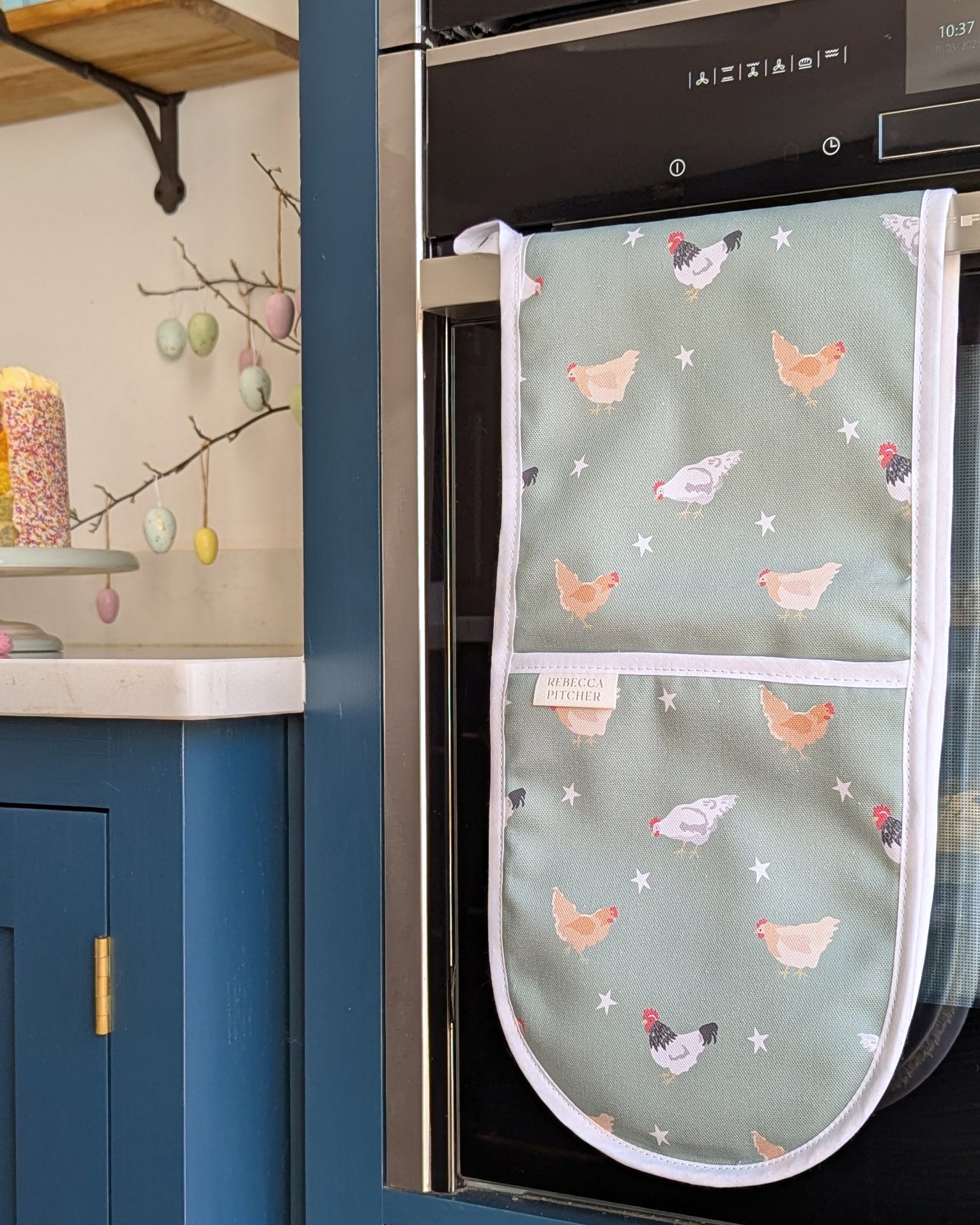 Oven mitt with chicken pattern hanging on a kitchen oven