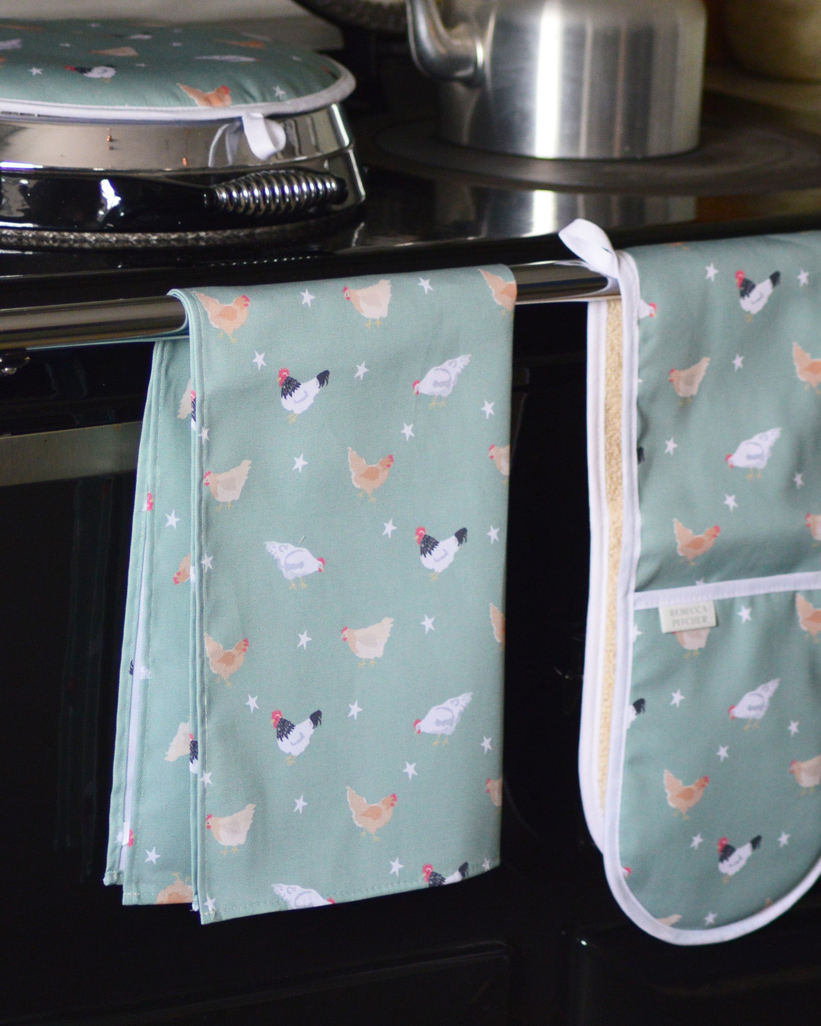 Green tea towel with chicken pattern hanging on a kitchen range cooker