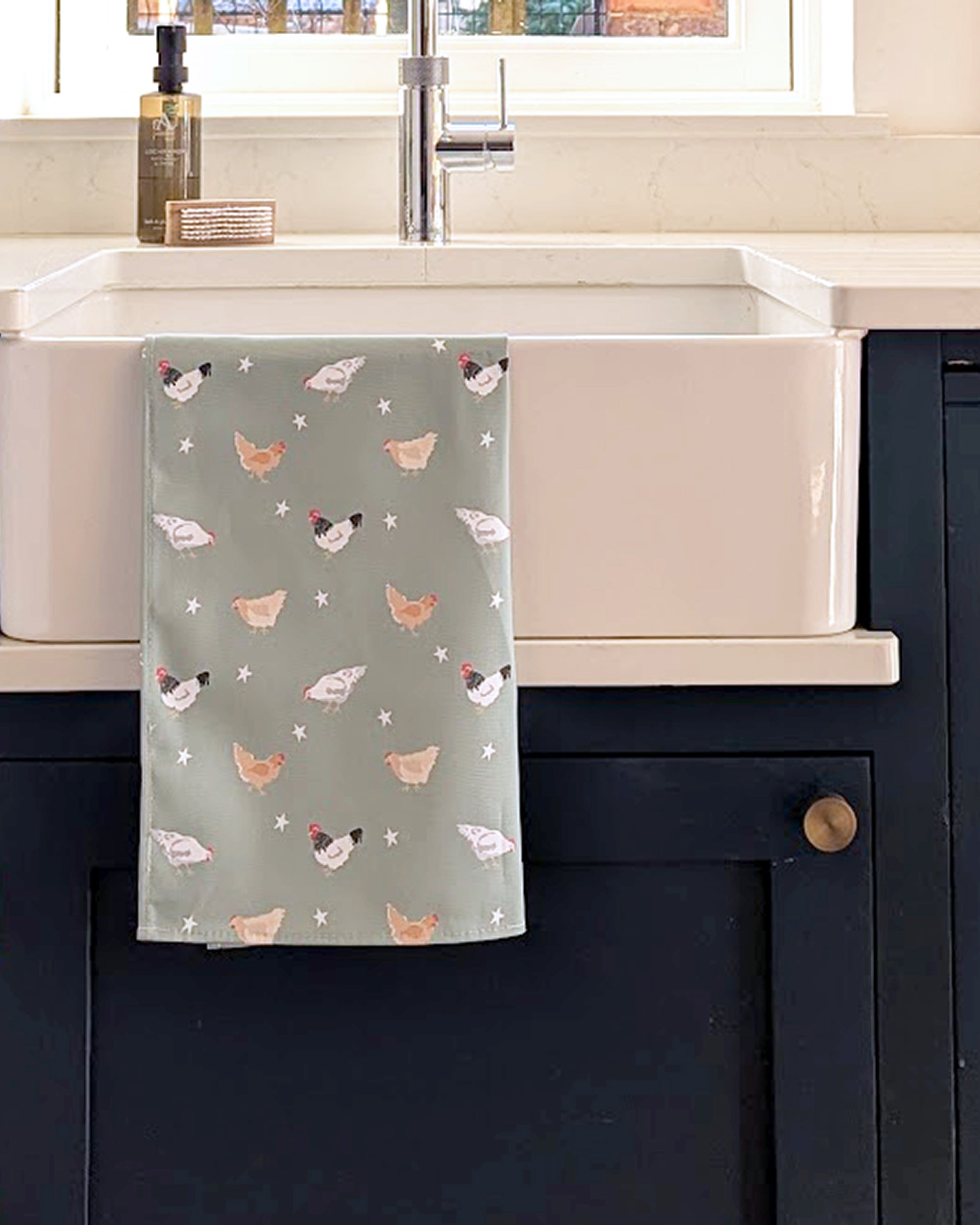 Kitchen towel with chicken pattern hanging on a cabinet next to a sink.