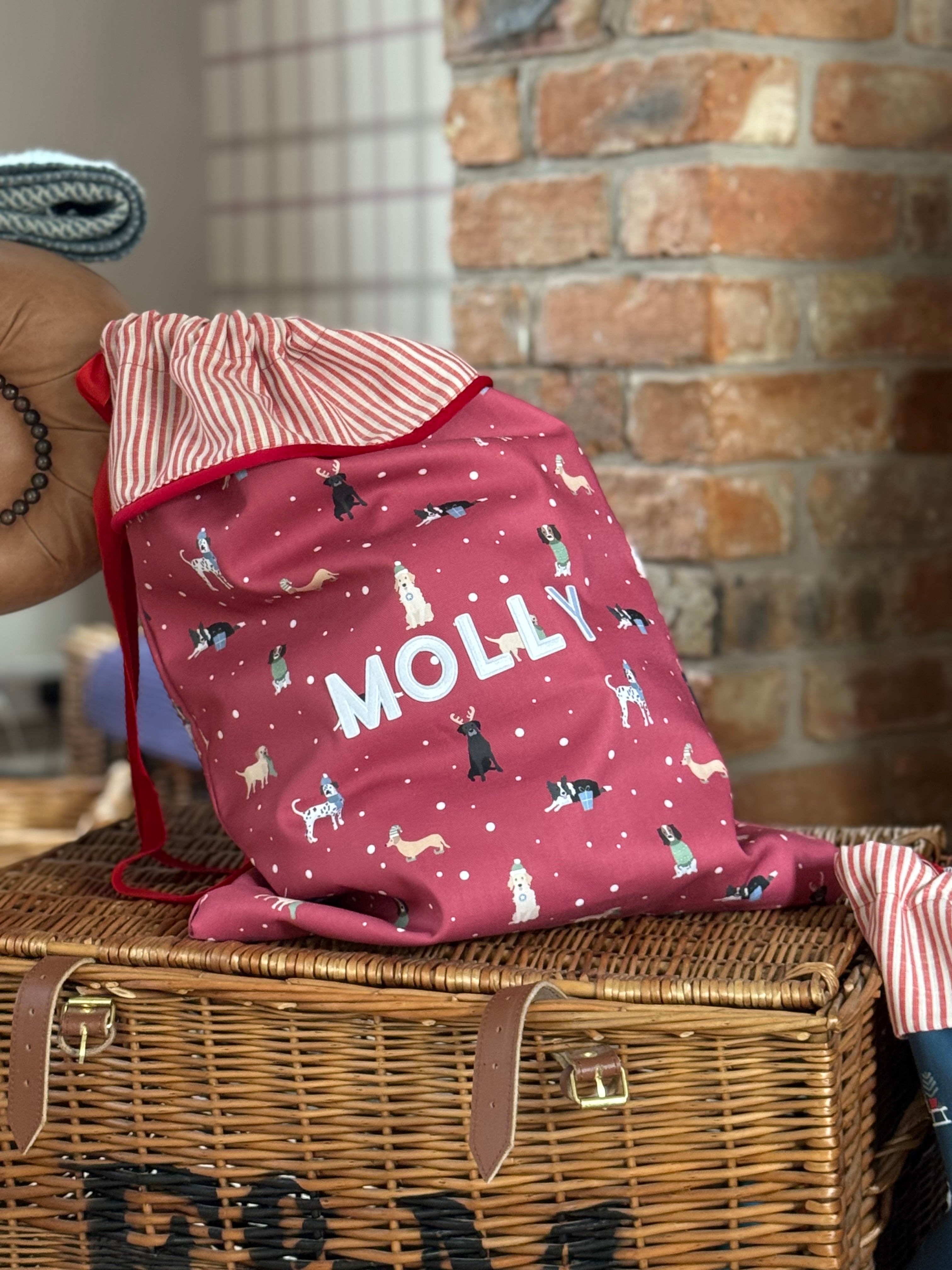 Red Christmas sack with dog pattern and 'MOLLY' text on a wicker basket against a brick wall.