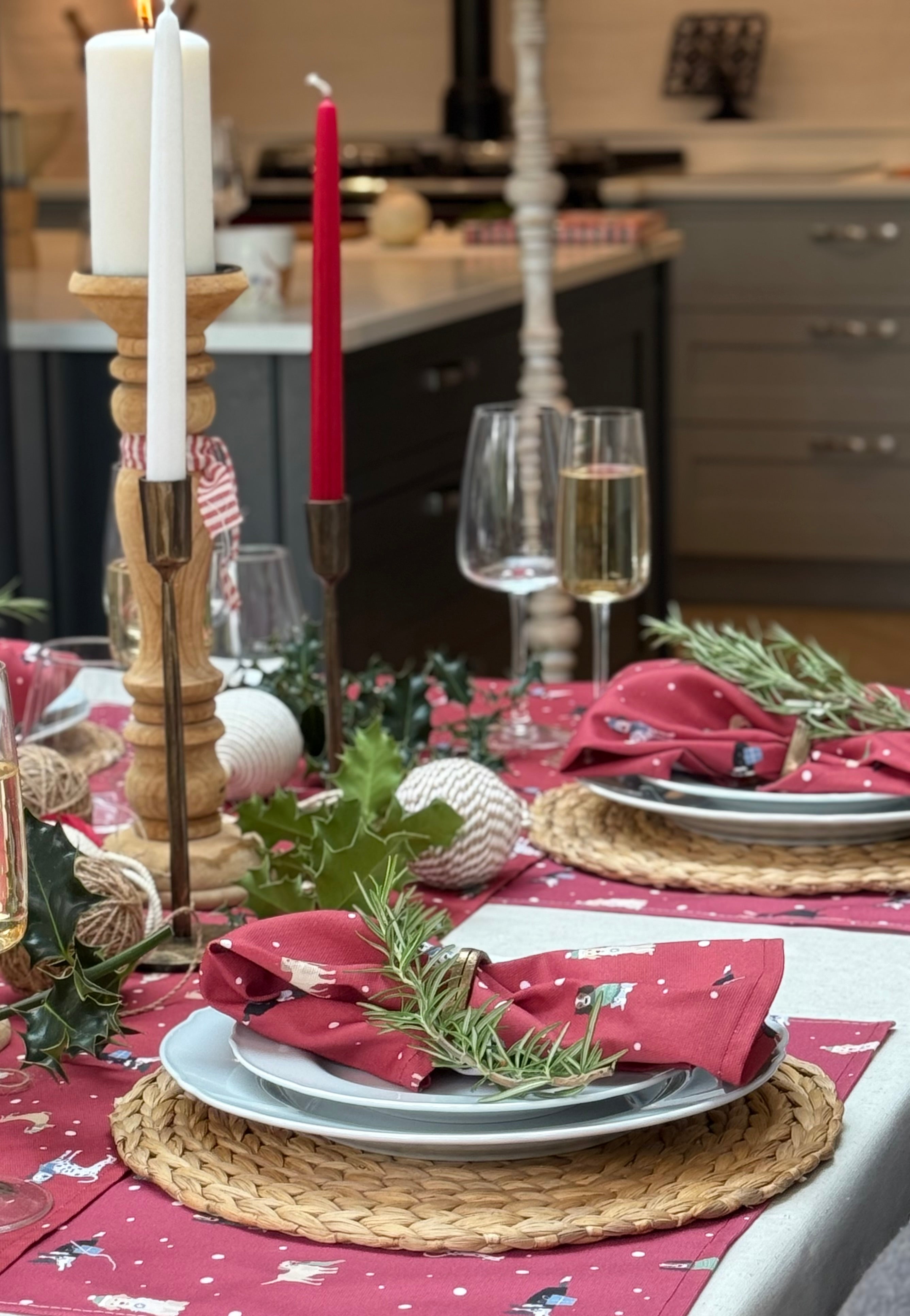 Christmas table setting with red Christmas Dogs placemats, napkins, candles, and decorative elements in a kitchen.