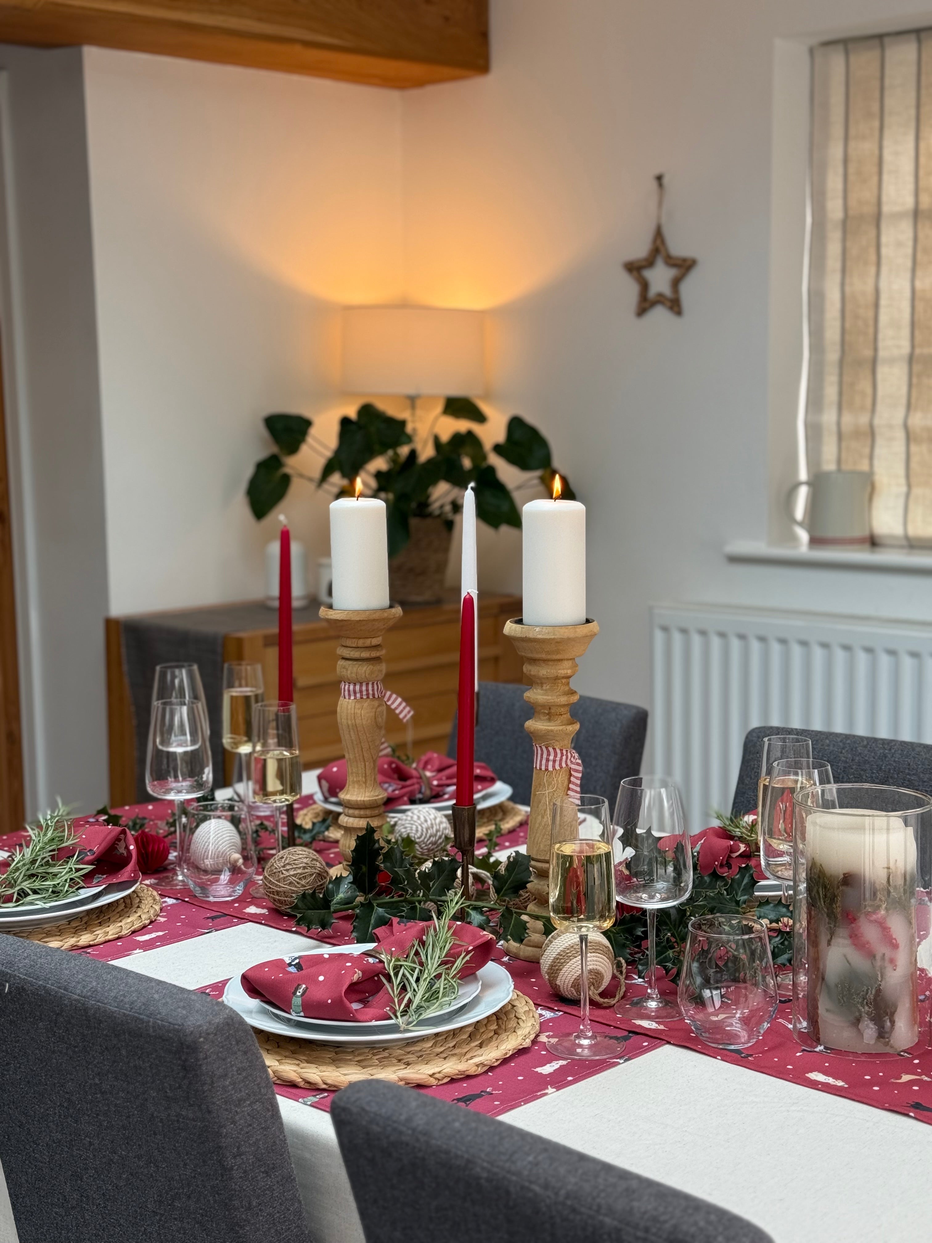 Dining table set for a meal with red Christmas Dogs design table runner, napkins and placemats in a cozy room.