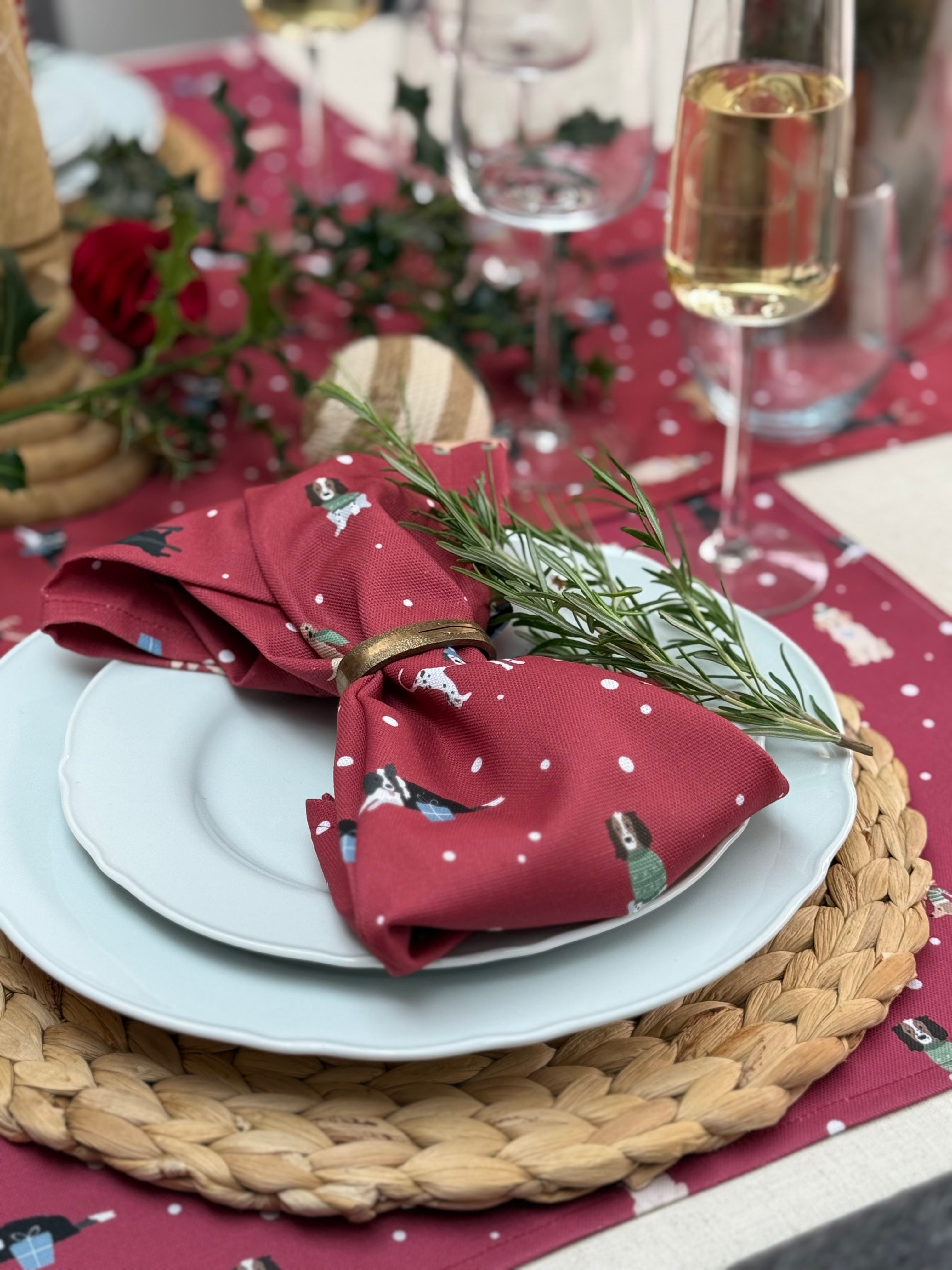 Decorative table setting with red christmas dogs napkin, white plates, and a glass of wine on a red tablecloth.