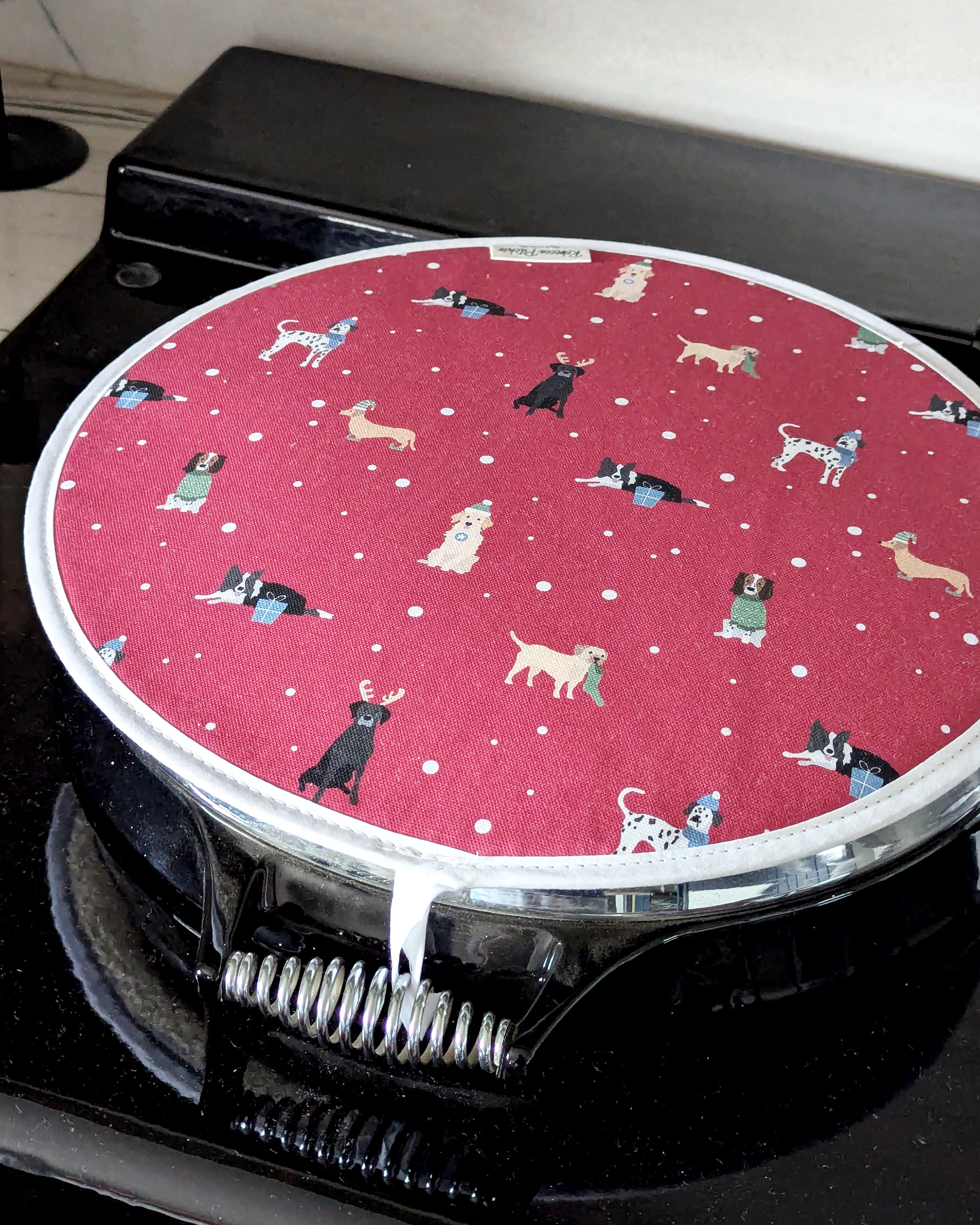 Round red hob cover with Christmas dogs pattern on a black range cooker