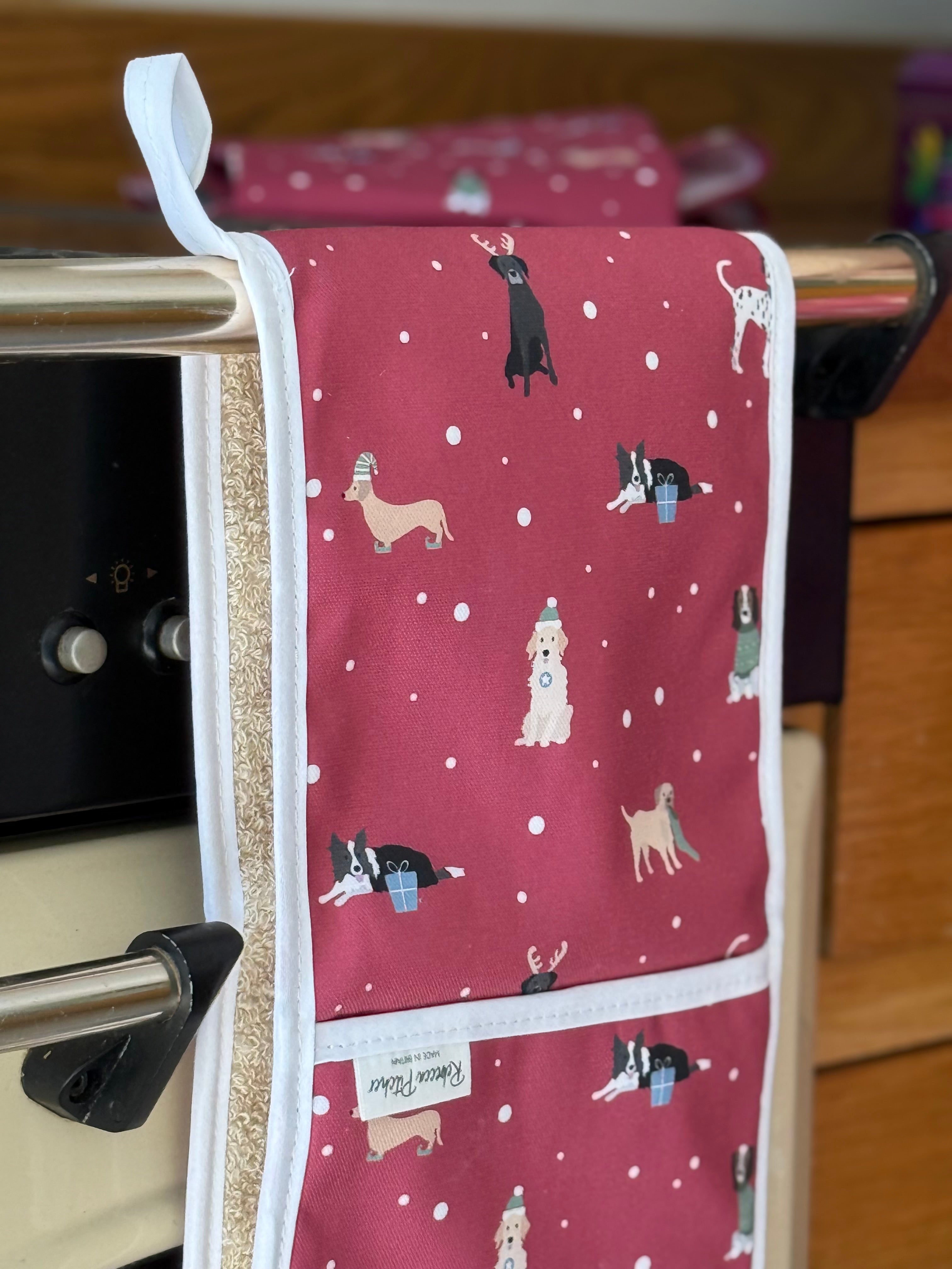 Red oven gloves with Christmas dog illustrations hanging on a kitchen cooker.