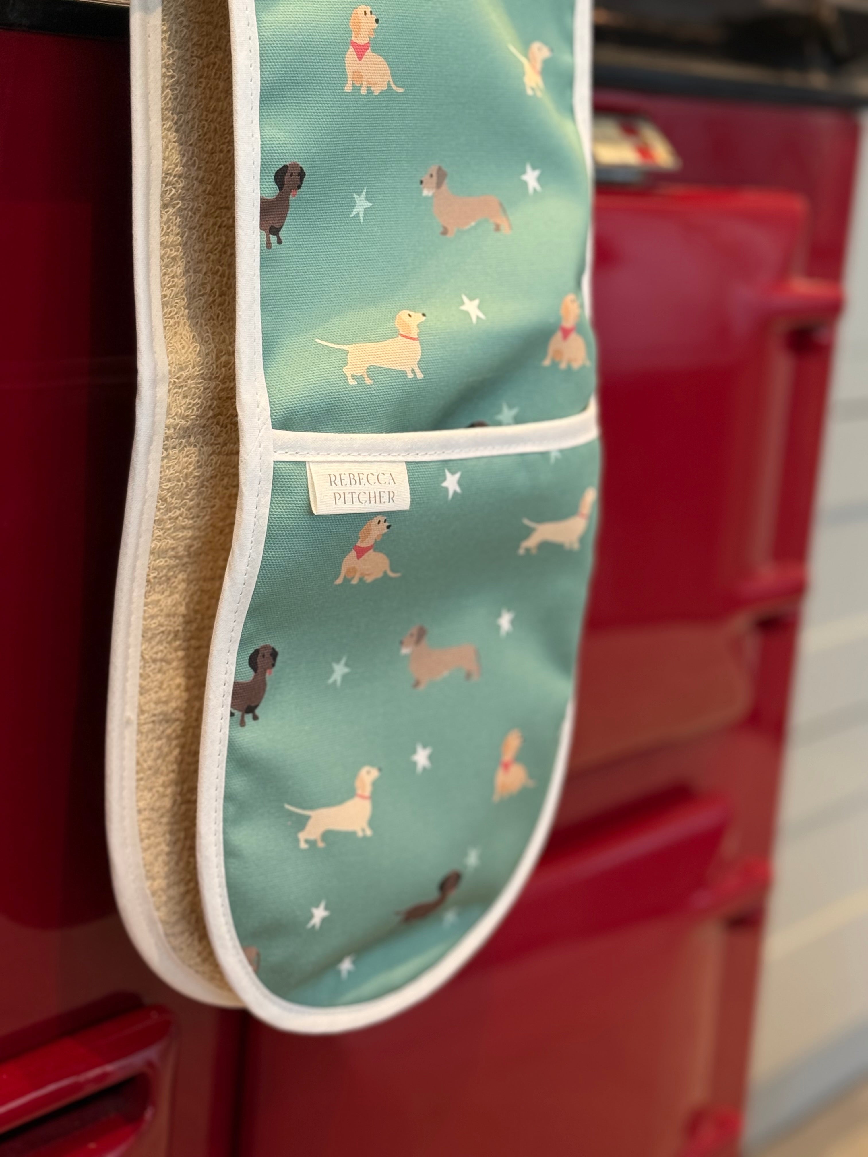 Oven mitt with dachshund dog pattern hanging on a red oven door