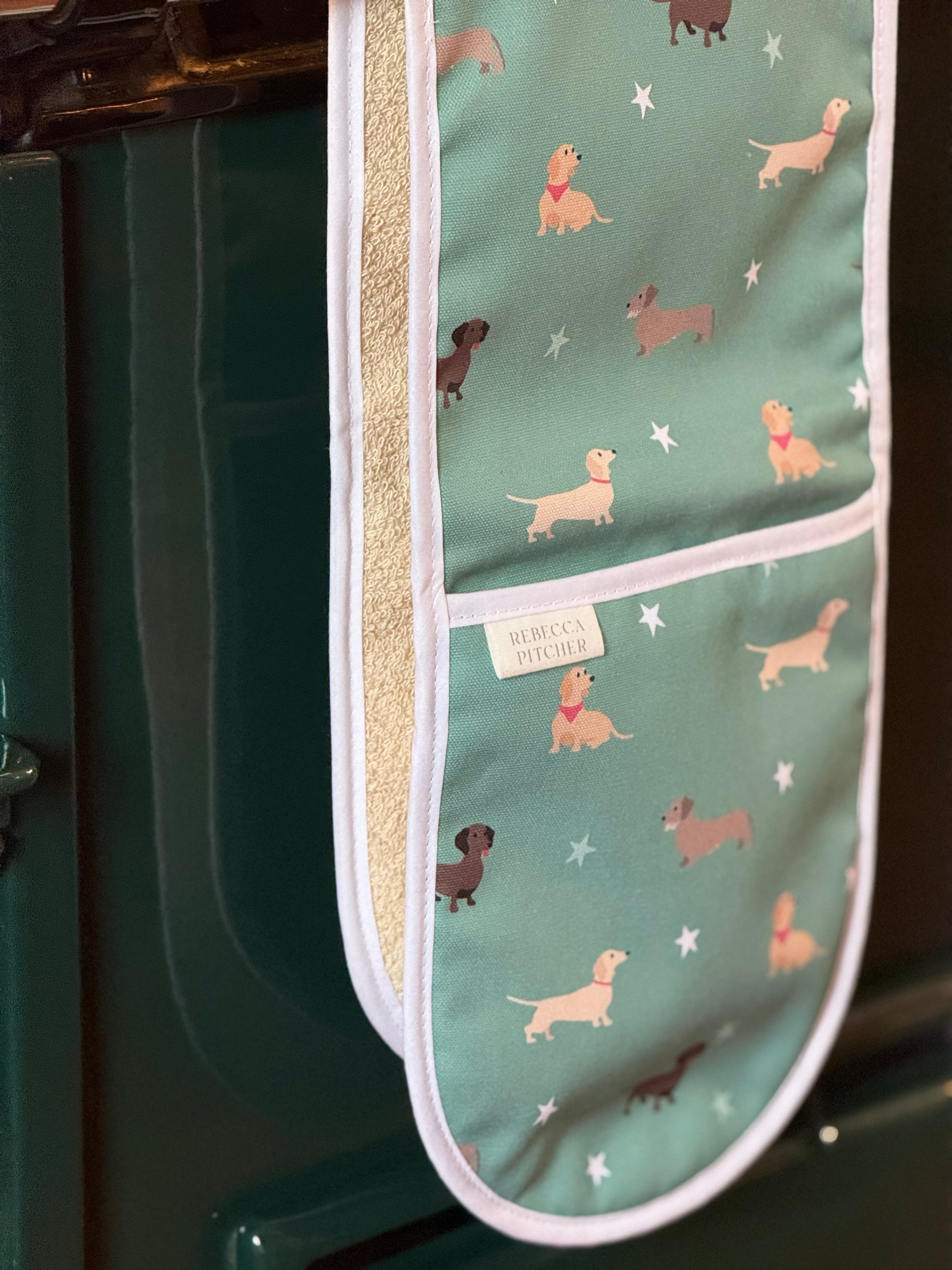 Oven mitt with dachshund dog pattern hanging on a green range cooker