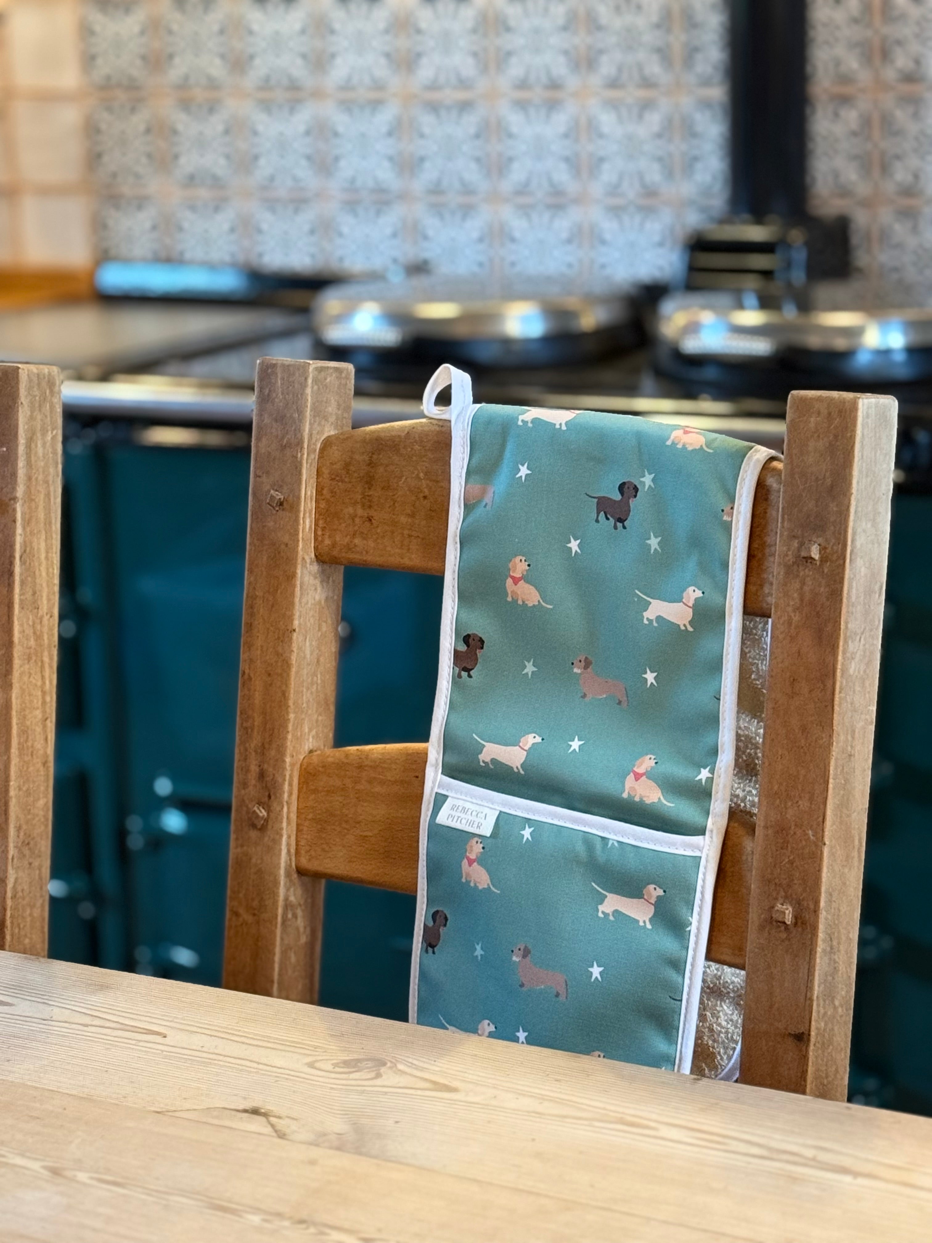 green oven gloves with dachshund dog pattern hanging on a wooden chair in a country kitchen.