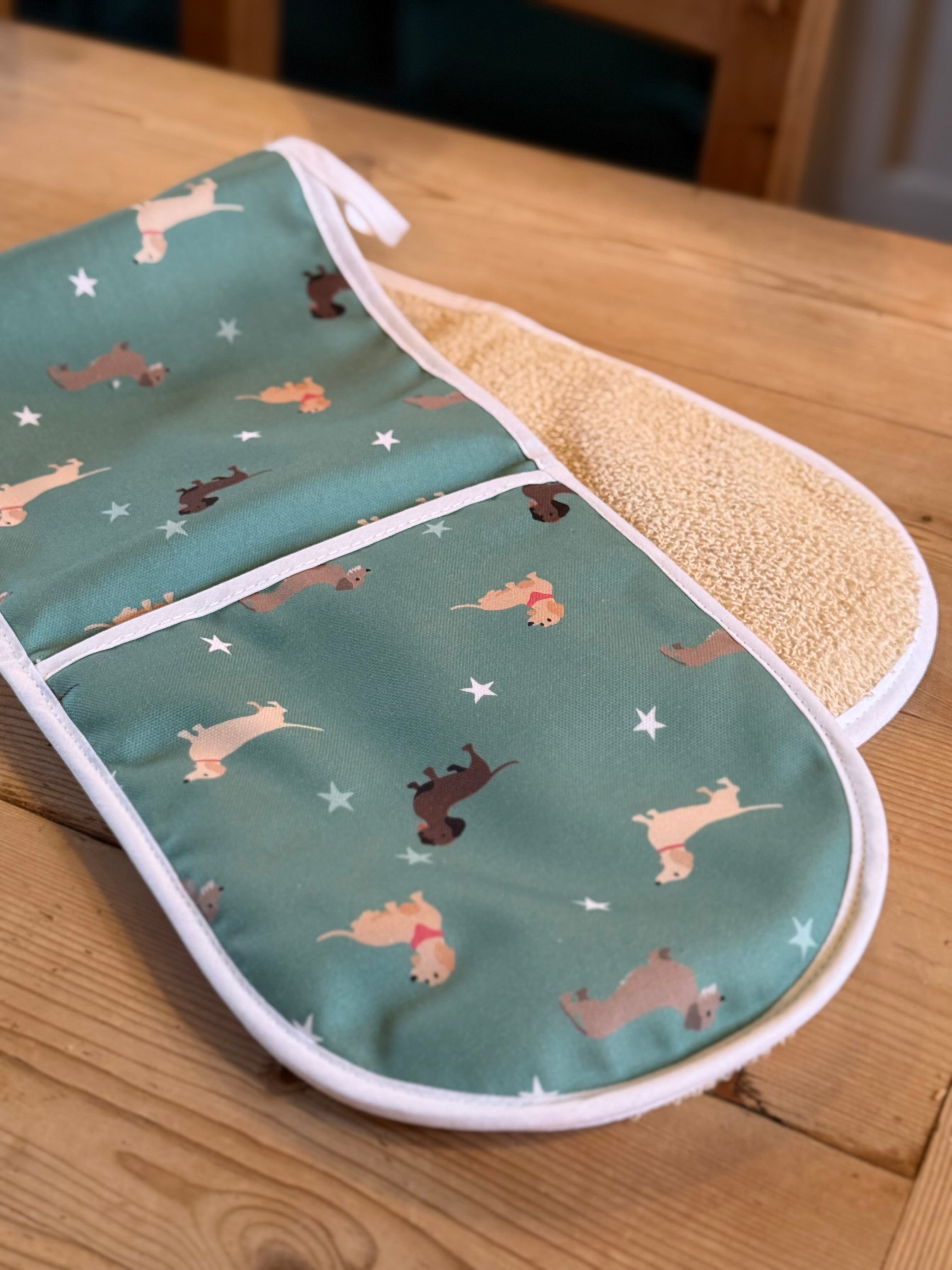 Green double oven gloves with a dachshund pattern on a wooden kitchen table