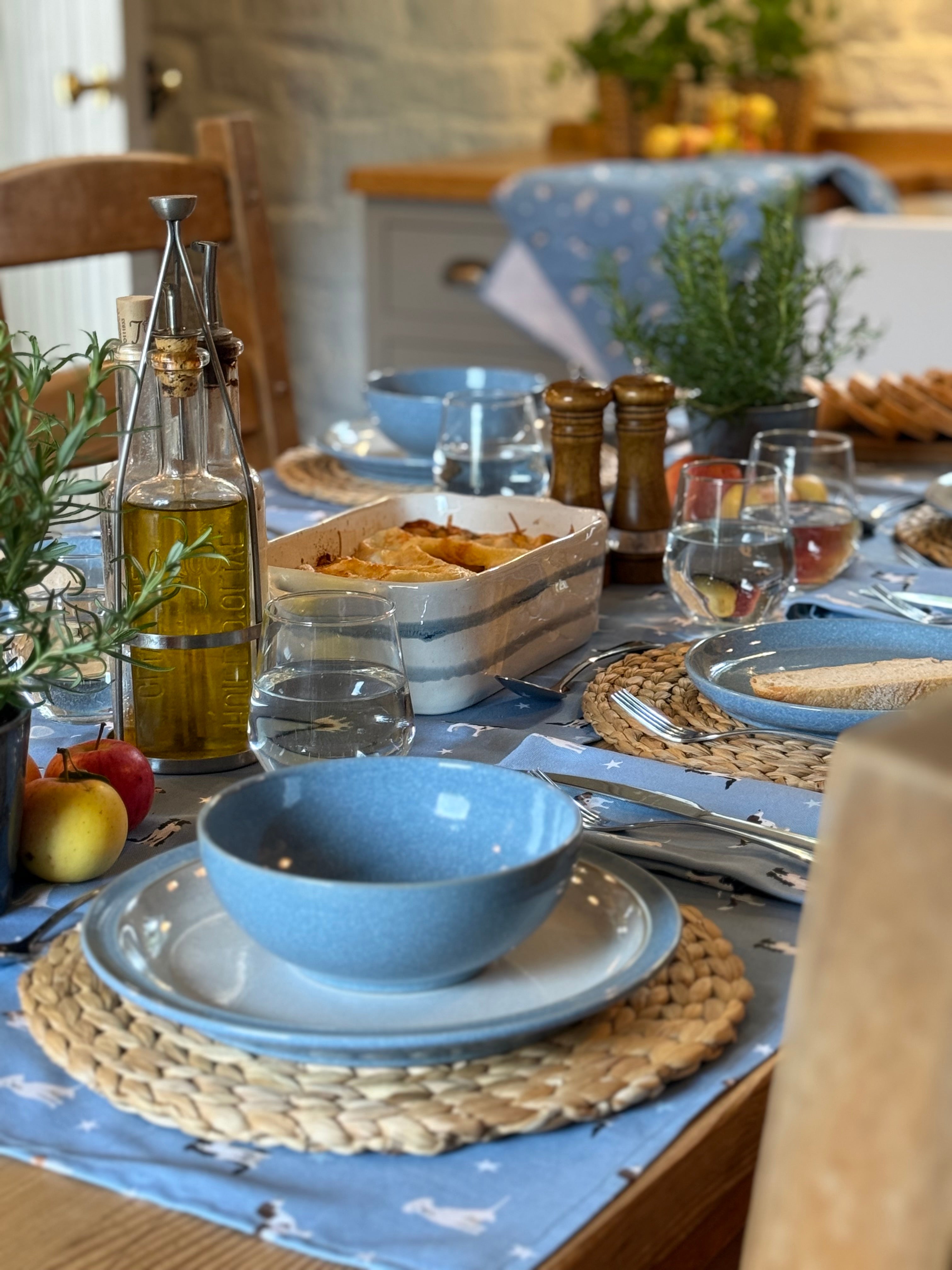 Dining table set with blue dog print table linens, glasses, and a variety of food items.