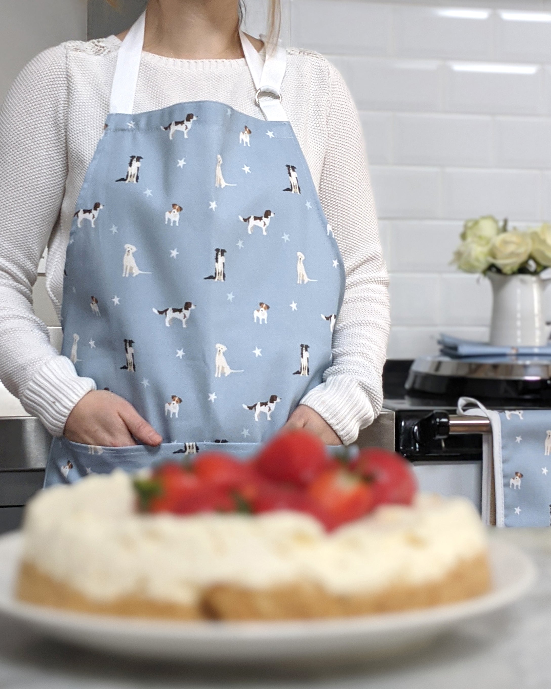 Person wearing a blue apron with dog patterns in a kitchen setting.