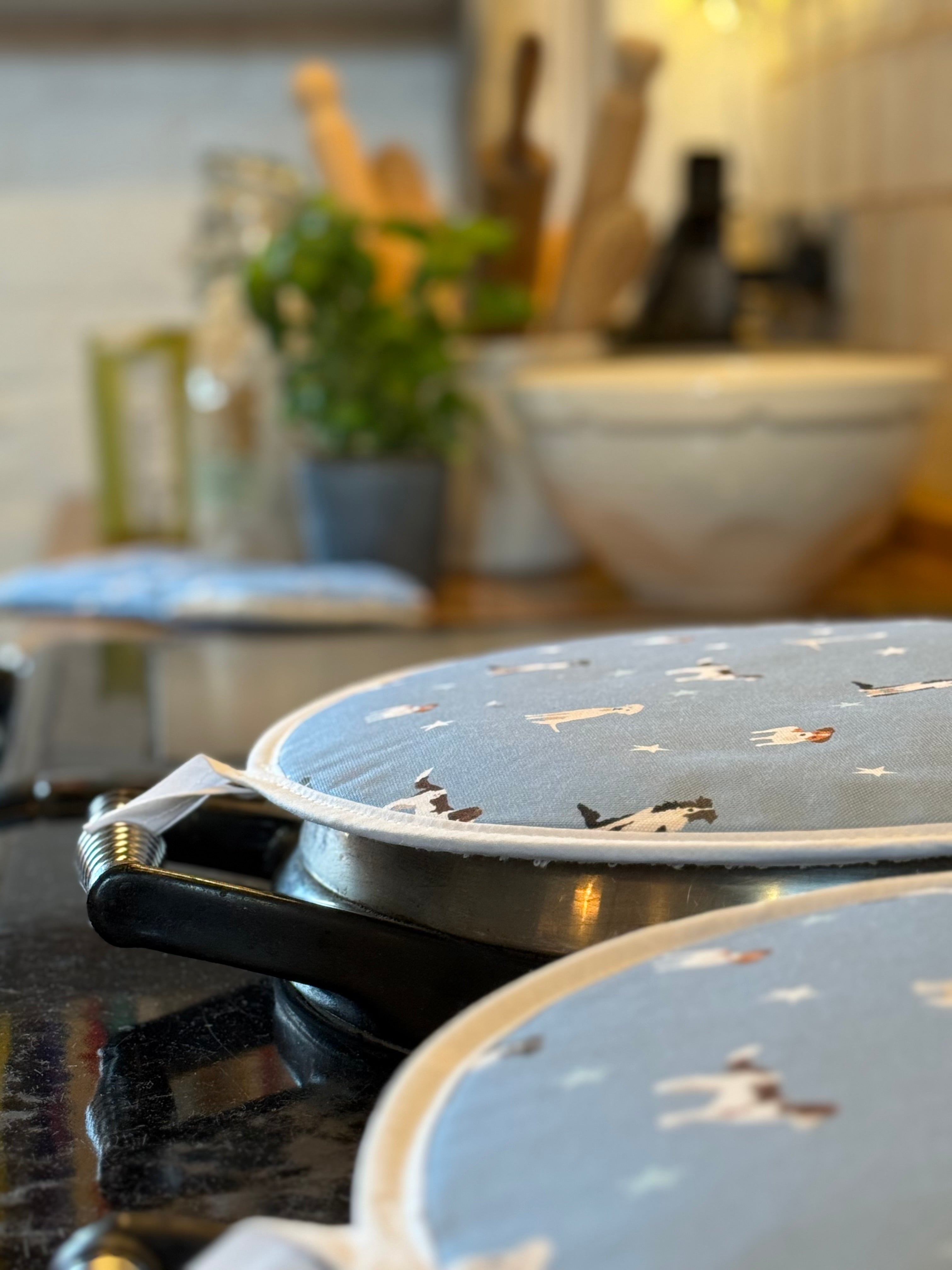 Two blue dog patterned hob covers on a kitchen stove with a blurred background of kitchen utensils and decor.
