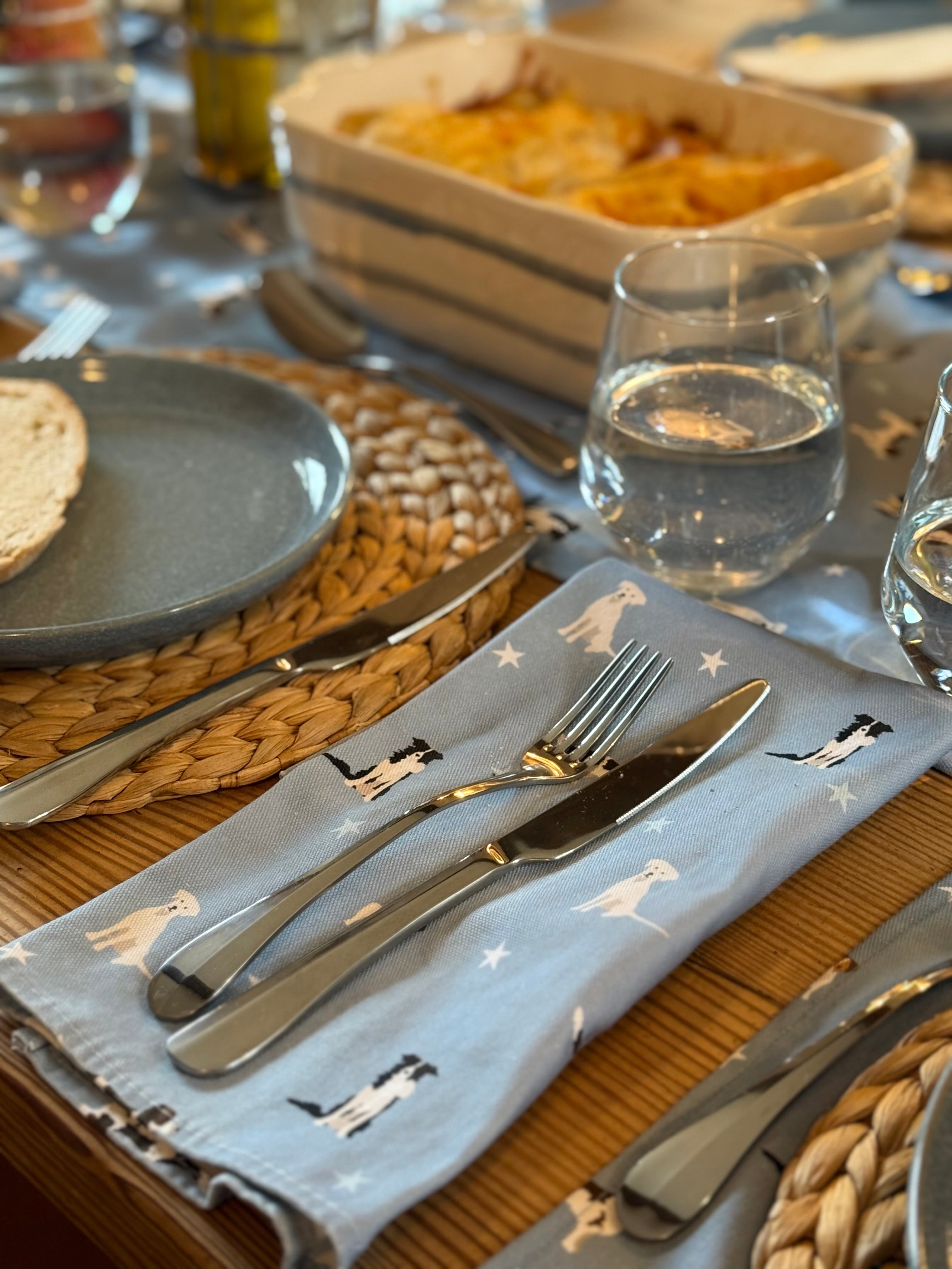 Dining table setting with plates, cutlery, and a blue napkin with dog prints.