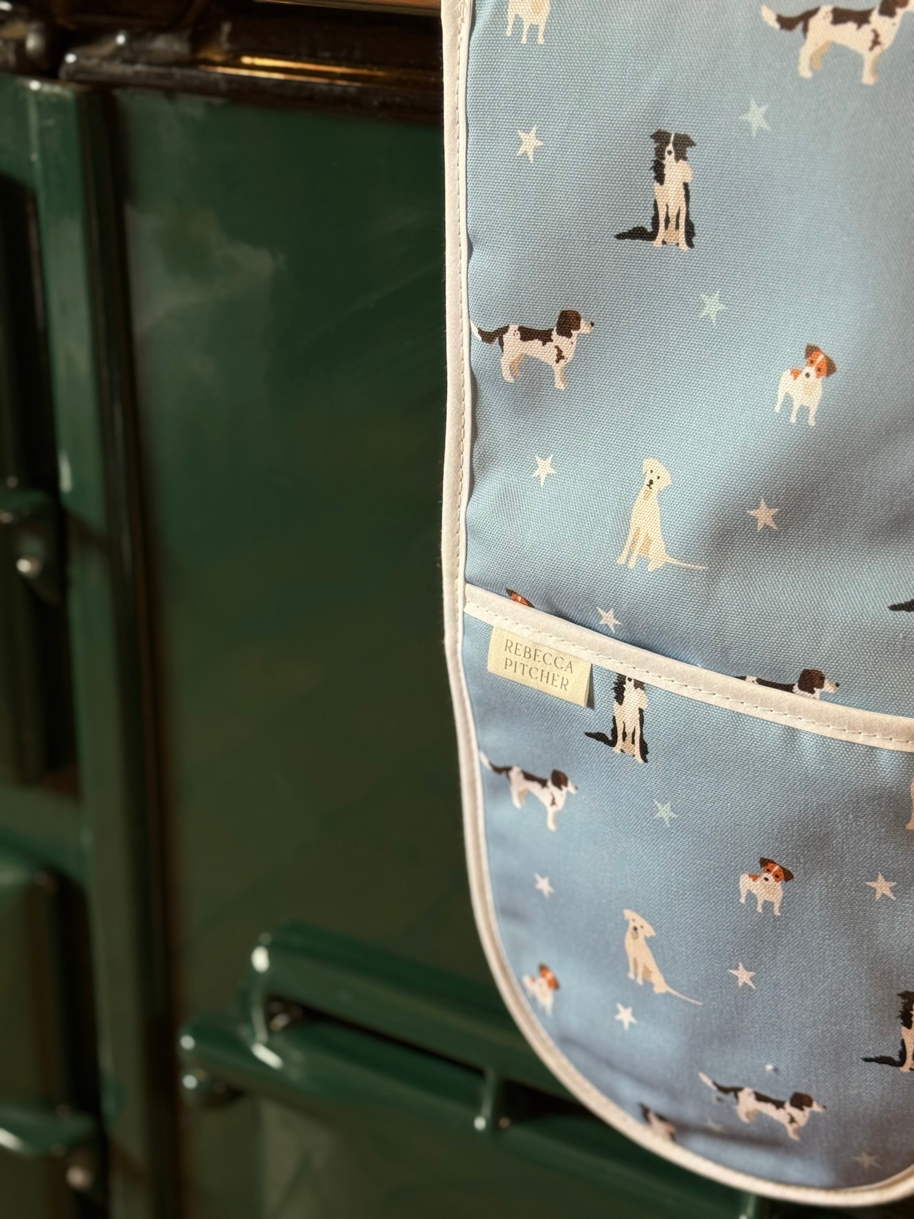 Oven mitt with dog pattern on a blue background, attached to a green oven.