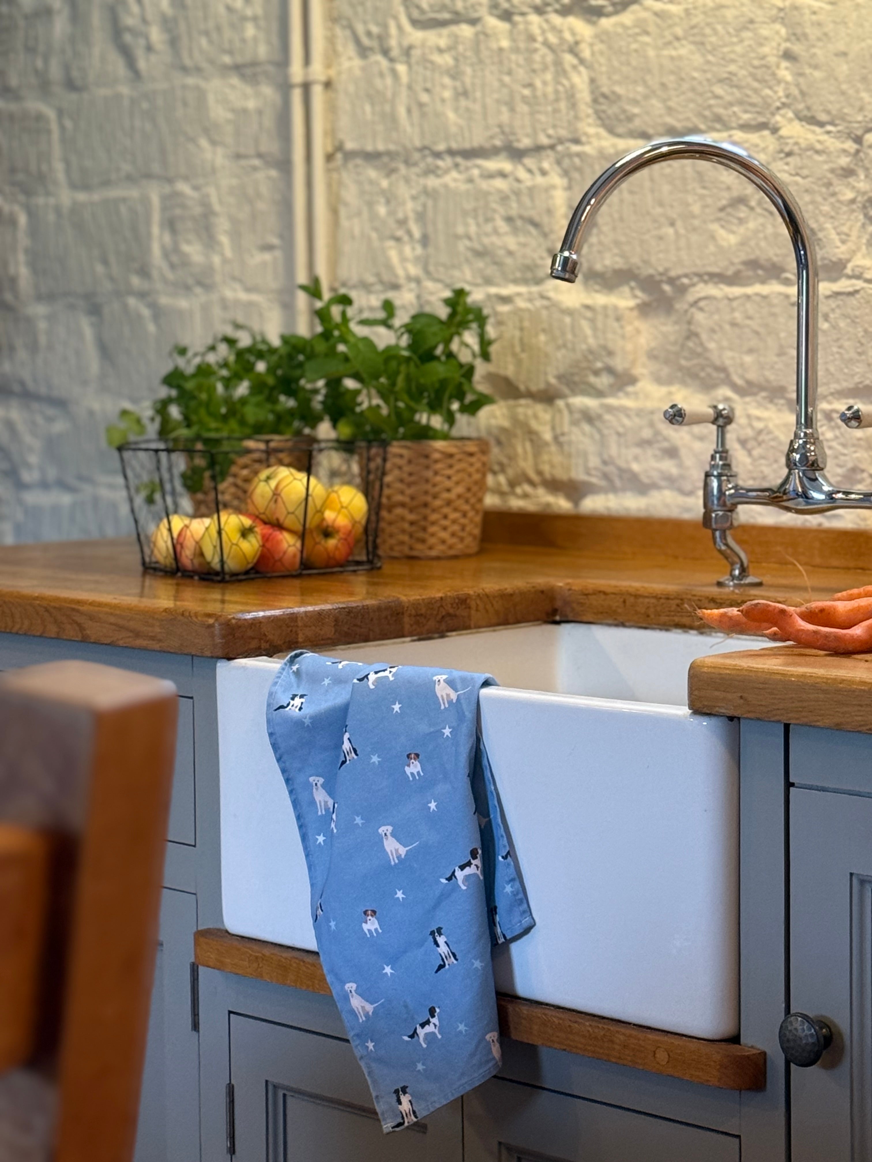 Kitchen sink with a blue dogs design tea towel draped over it, wooden countertop, and stone wall background.