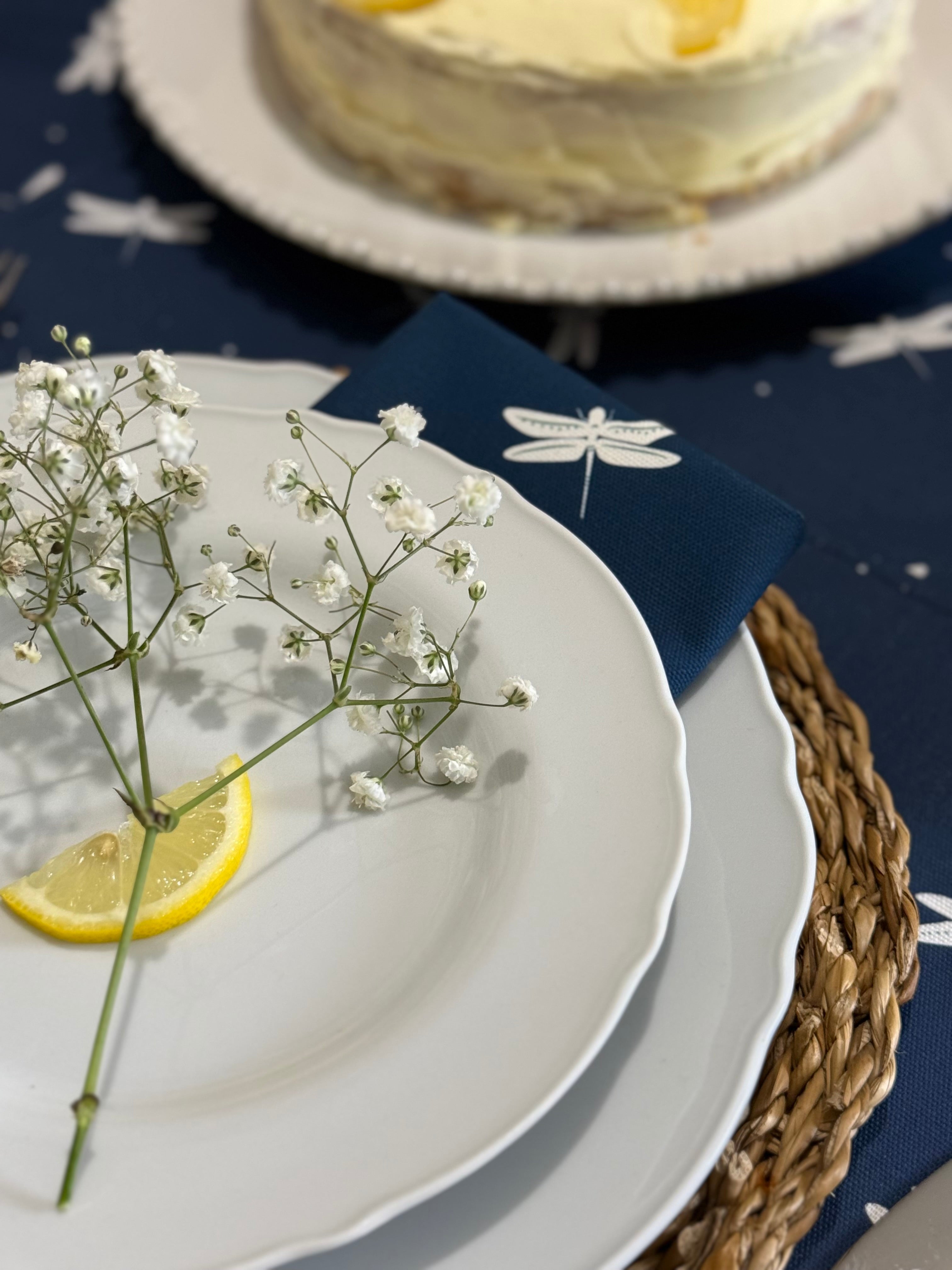 Close-up of a table setting with a white plate, lemon wedge, baby's breath, and dragonfly napkins