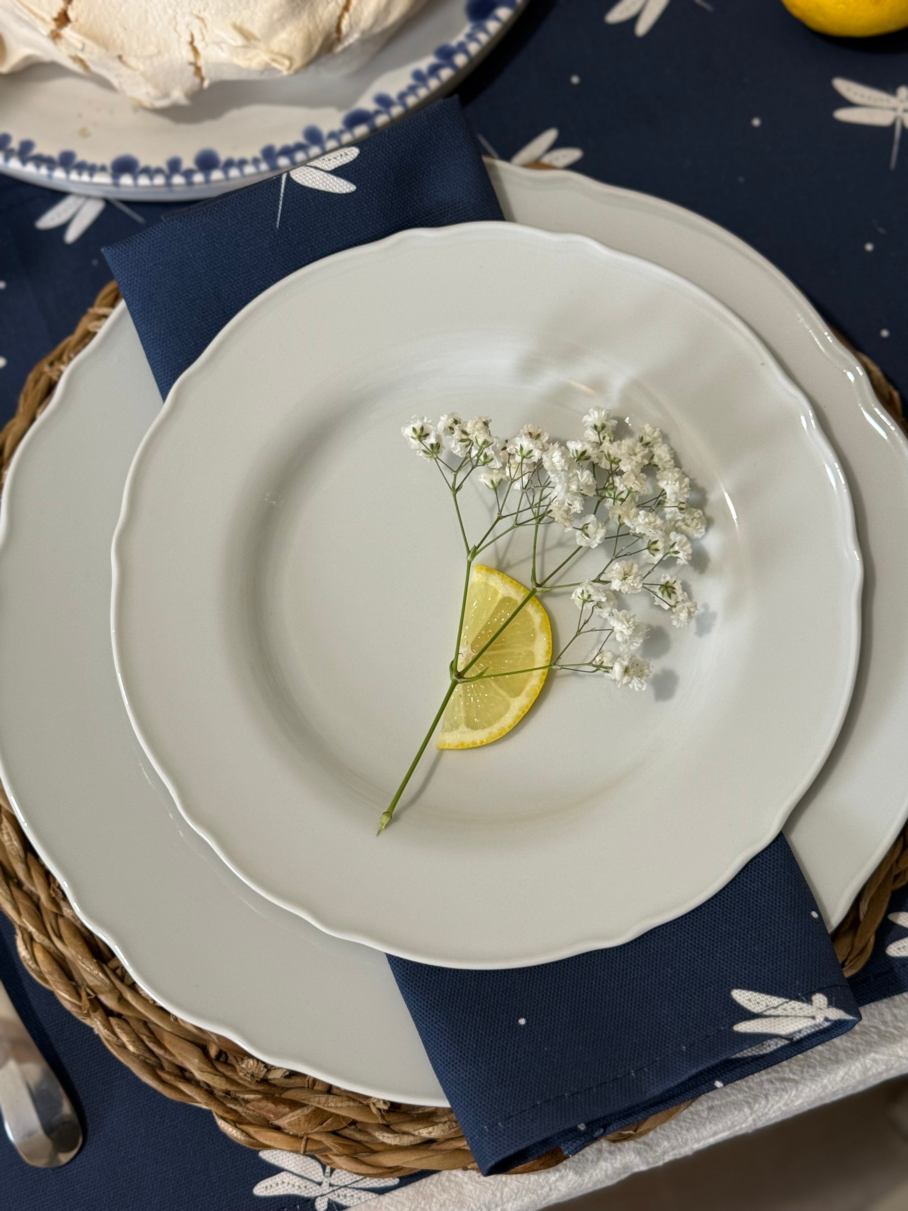 White plate with a lemon wedge and baby's breath on a navy blue cotton napkin with dragonfly patterns.