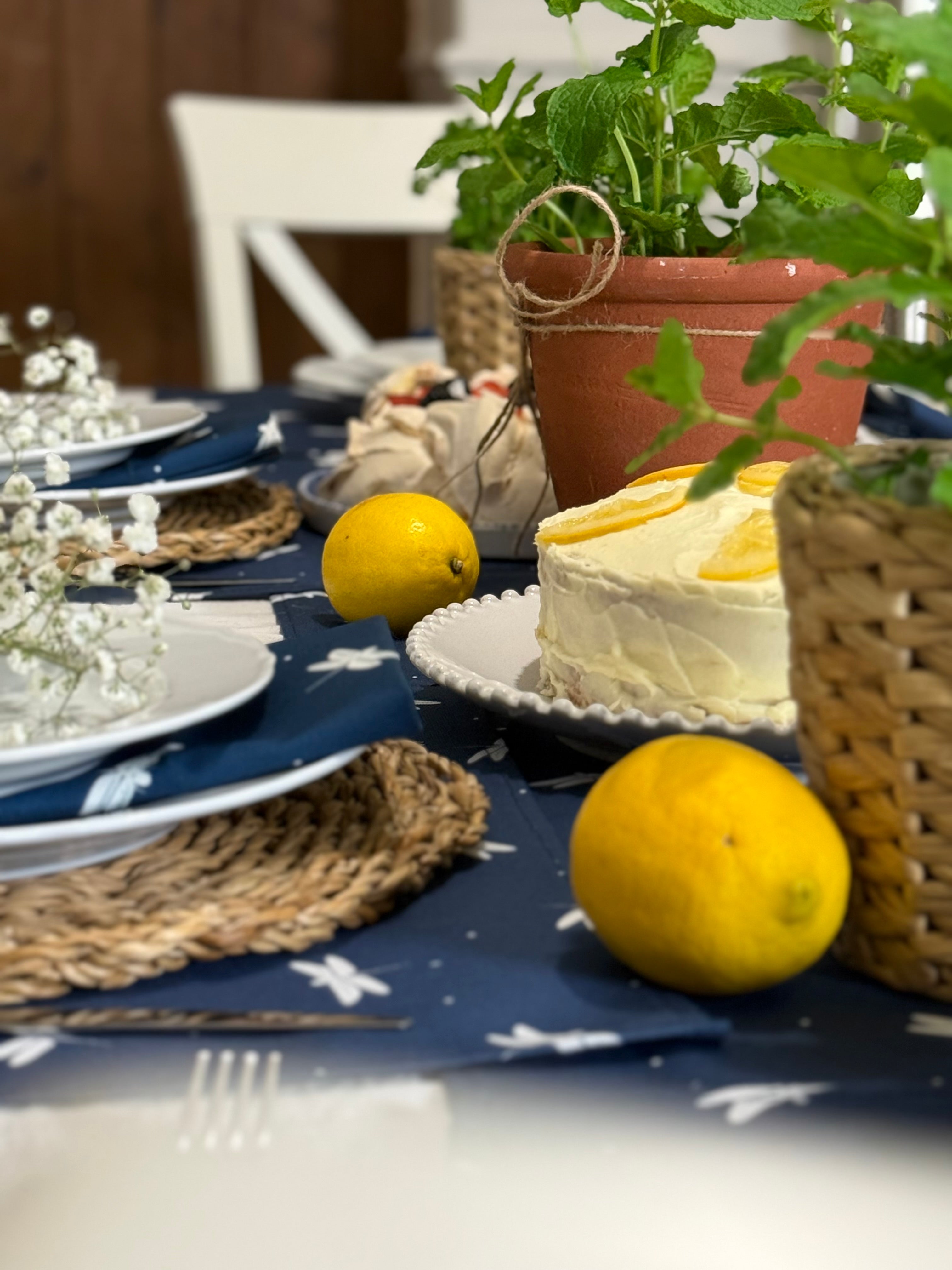 Table setting with a cake, lemons, and plants on a navy blue table runner
