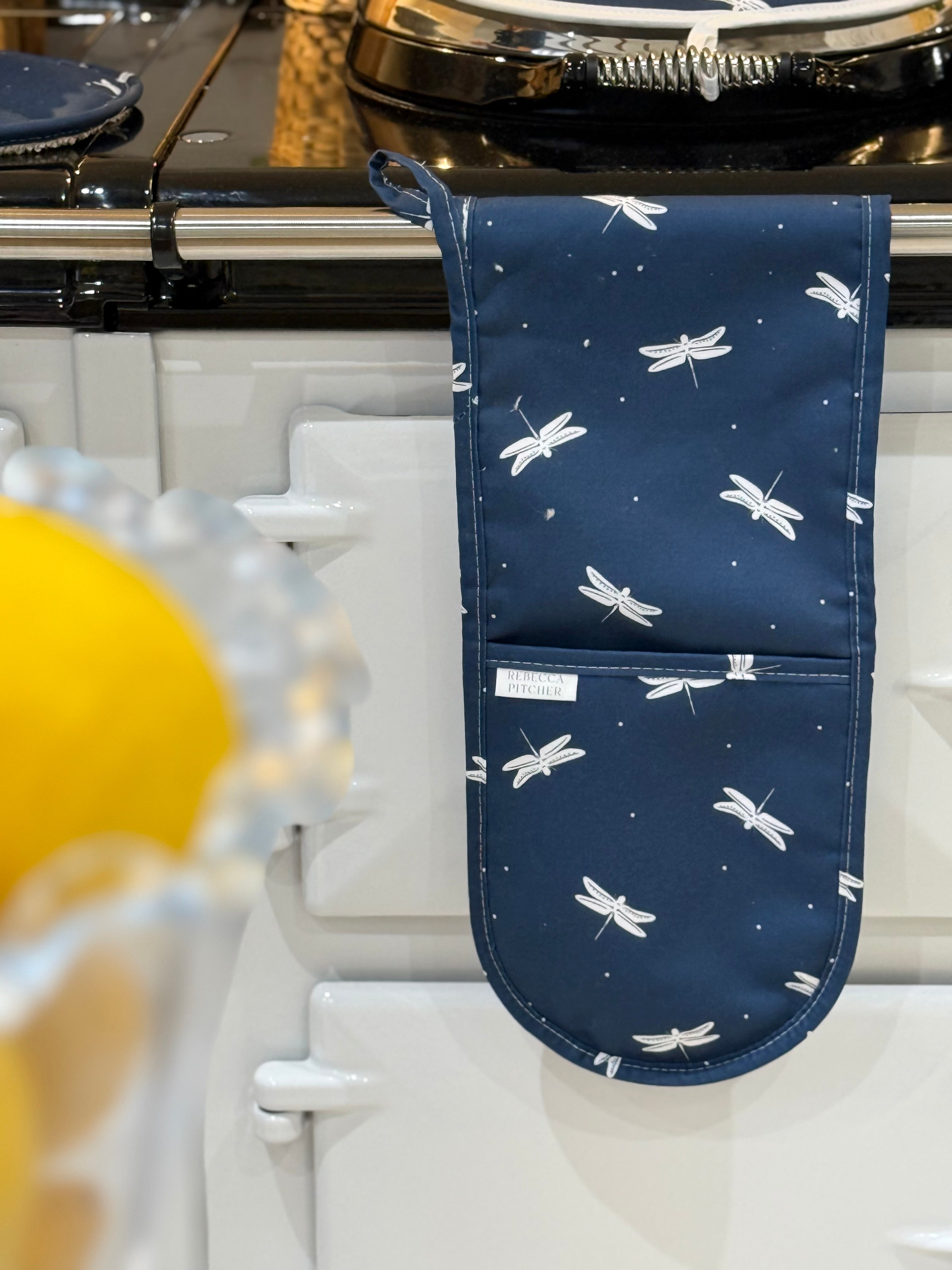 Navy oven mitt with white dragonfly pattern hanging on a stove.