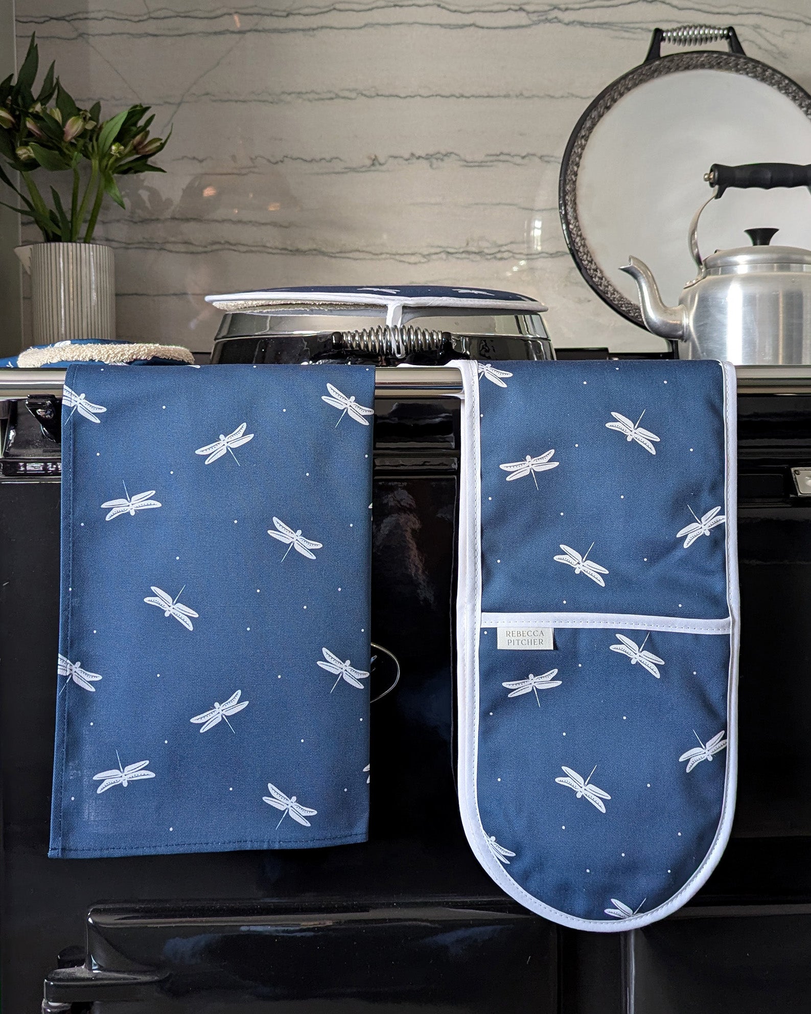 Navy blue tea towel and oven mitt with dragonfly pattern hanging on a stove.