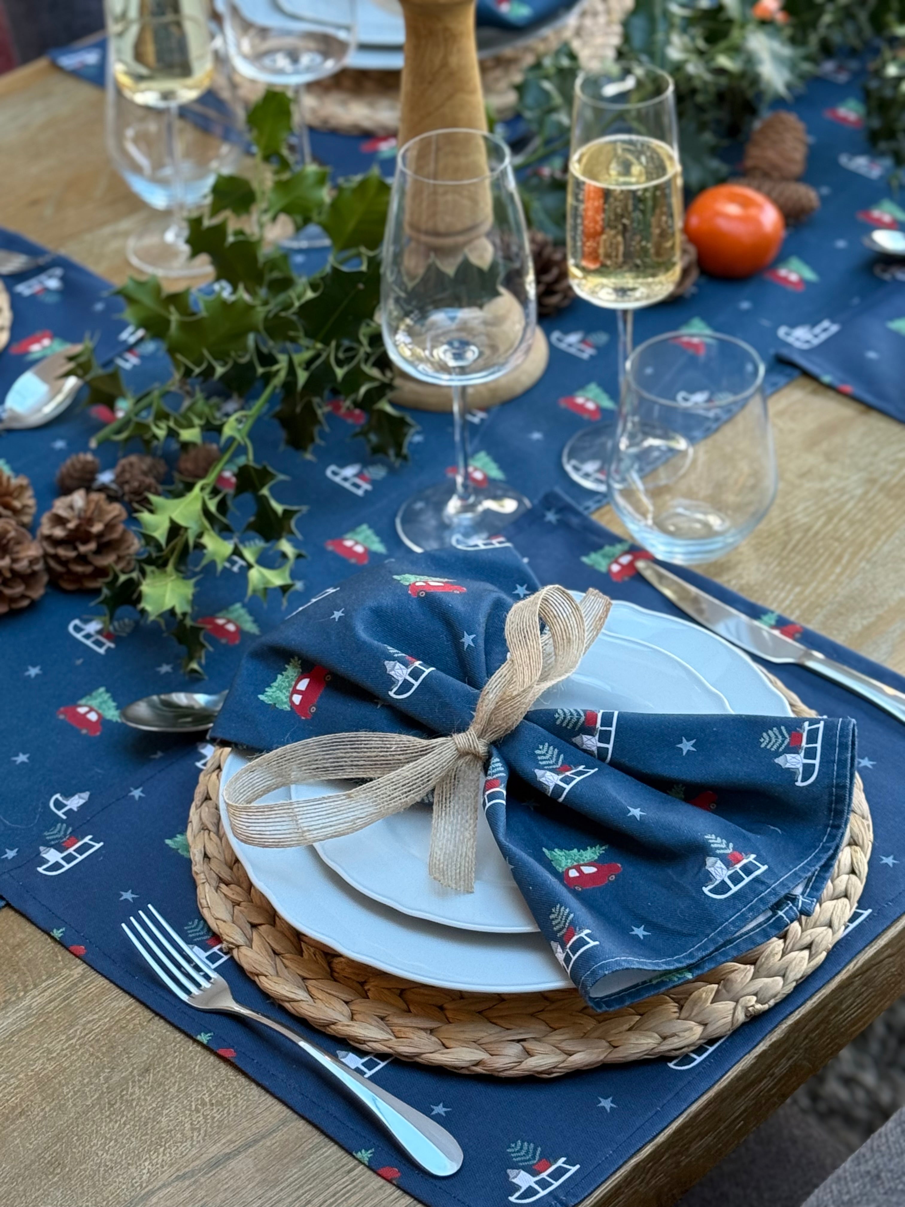 Christmas-themed table setting with navy placemats, white plates, and decorative napkins.