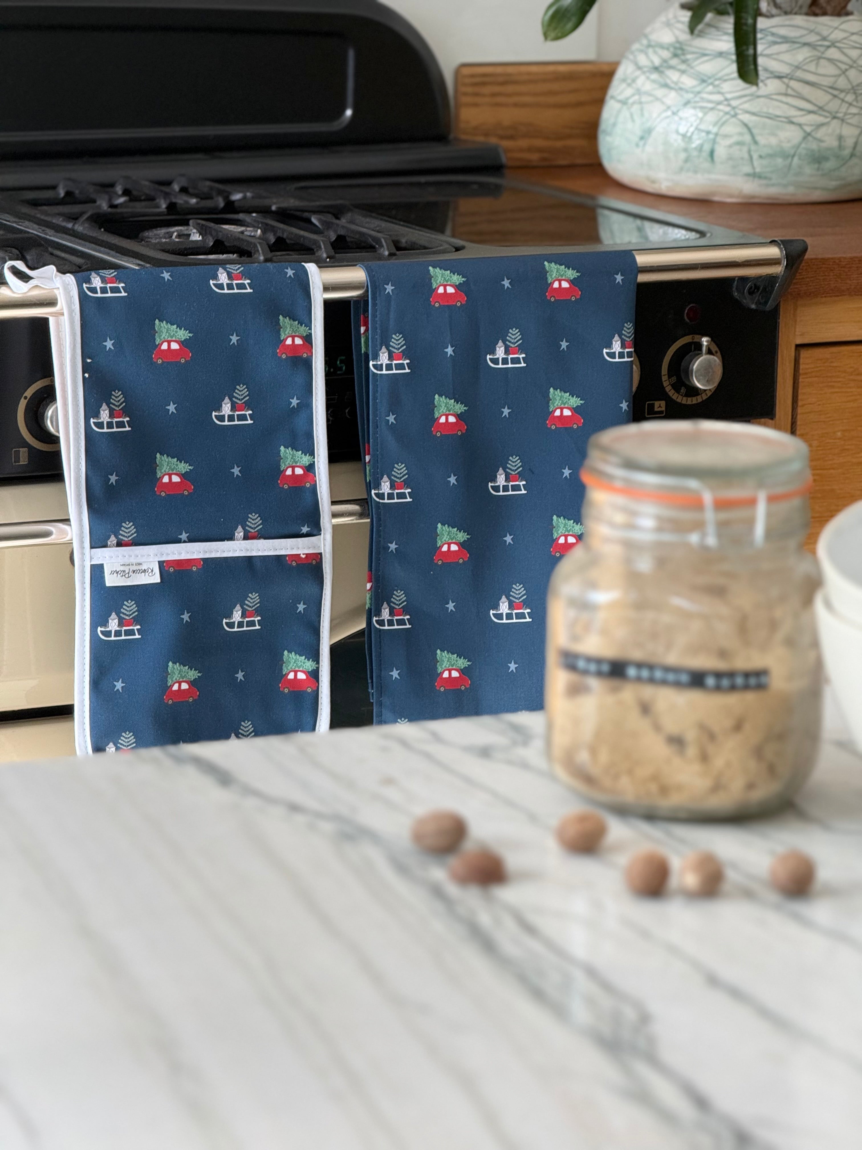 Kitchen towel with Christmas Car and tree pattern hanging on a stove, next to a jar of brown sugar.