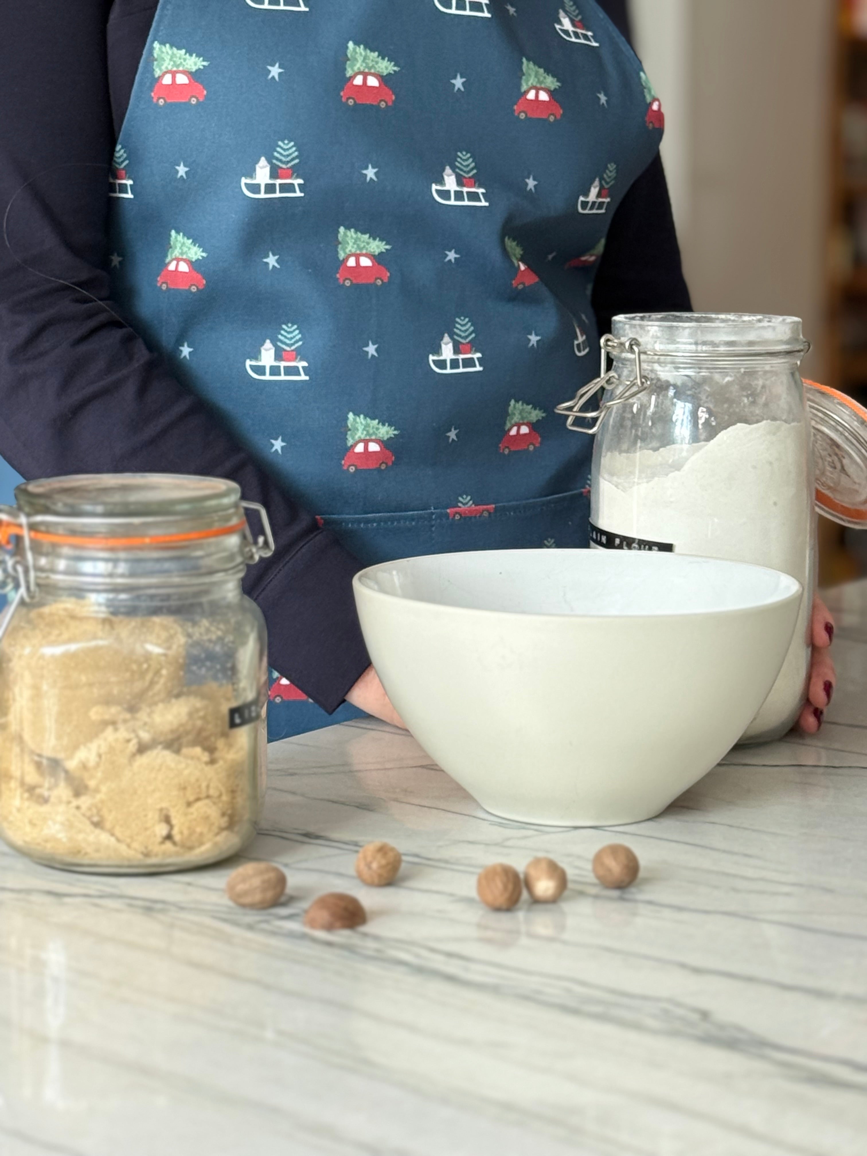 Person wearing a festive apron with baking ingredients on a marble countertop