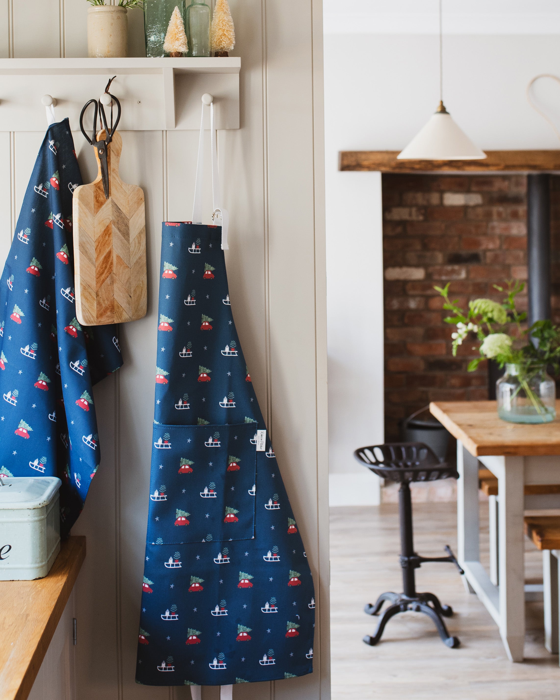 Blue apron with red and white christmas patterns hanging on a hook in a kitchen.