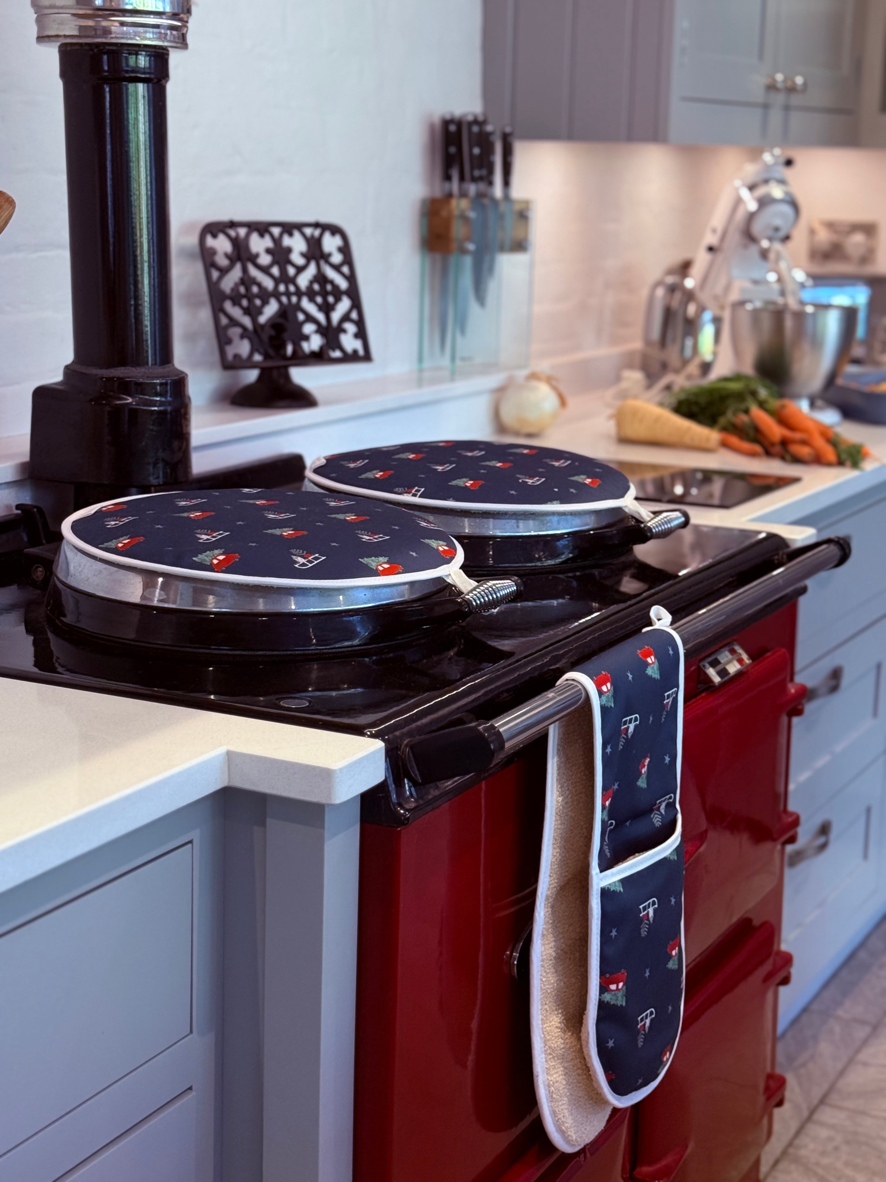 Red Aga range cooker with navy blue Christmas design hob covers and oven mitts in a kitchen setting.