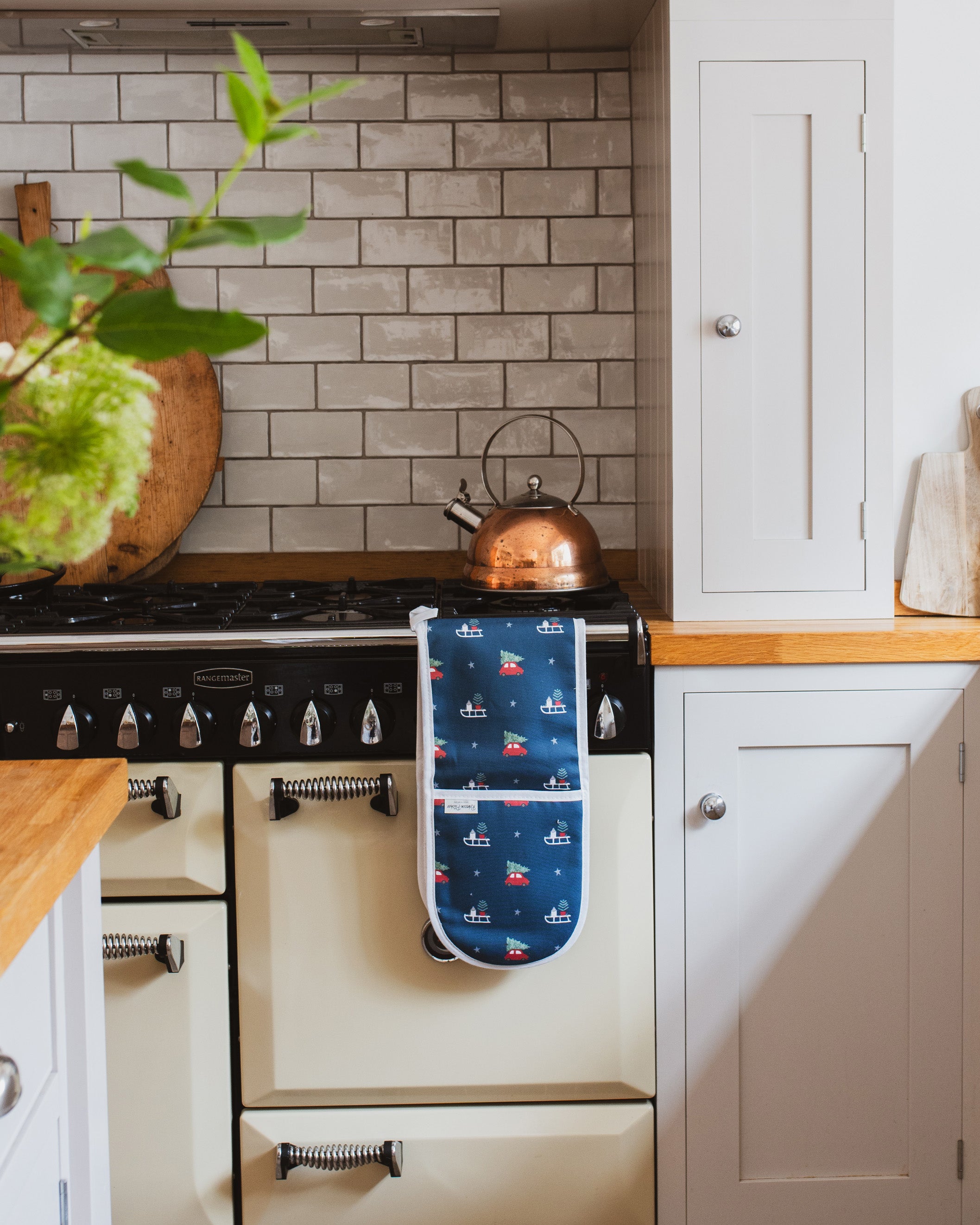 Navy Blue Christmas pattern oven gloves hanging on a range cooker rail in a kitchen setting