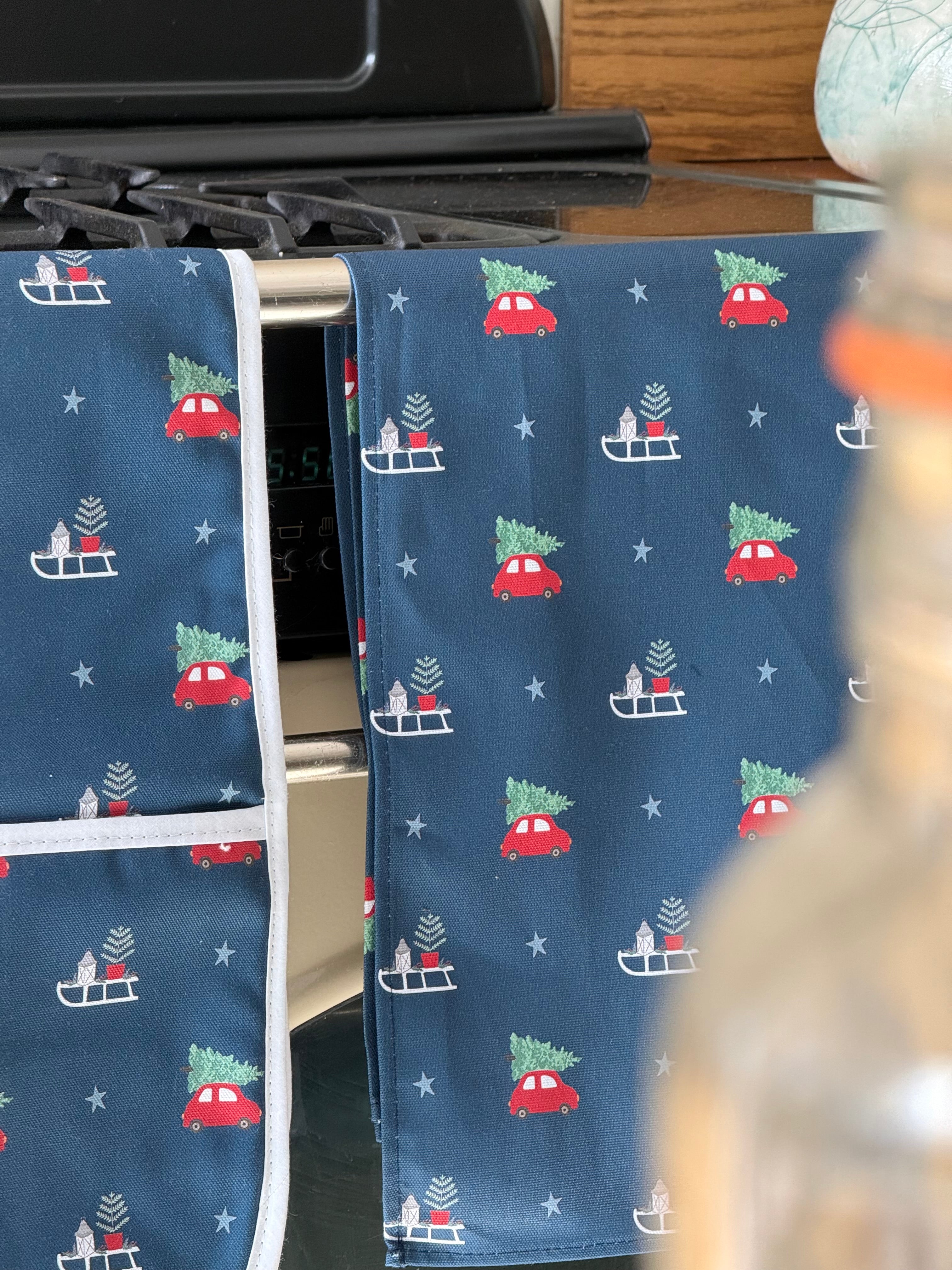 Navy blue kitchen towels with Christmas car and tree pattern hanging on a stove.