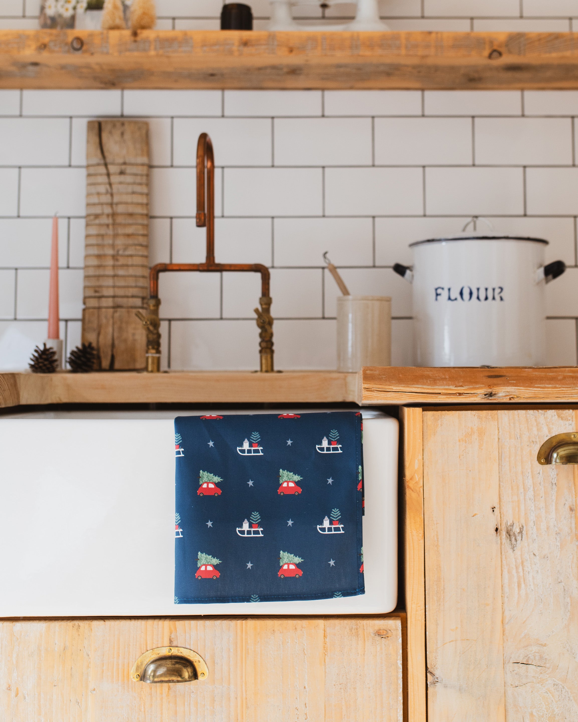 Christmas-themed towel on a kitchen sink with wooden cabinets and white tiled wall.
