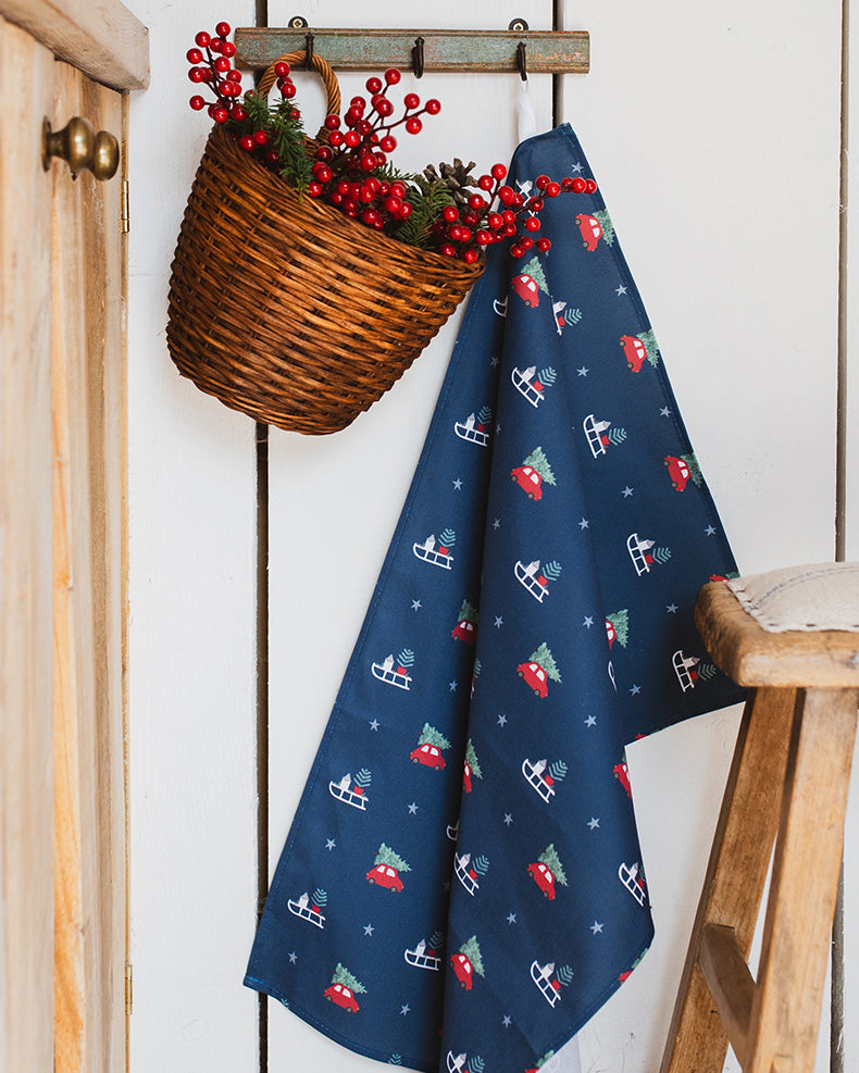 Navy blue towel with Christmas-themed pattern hanging on a wooden hook with a basket of red berries.