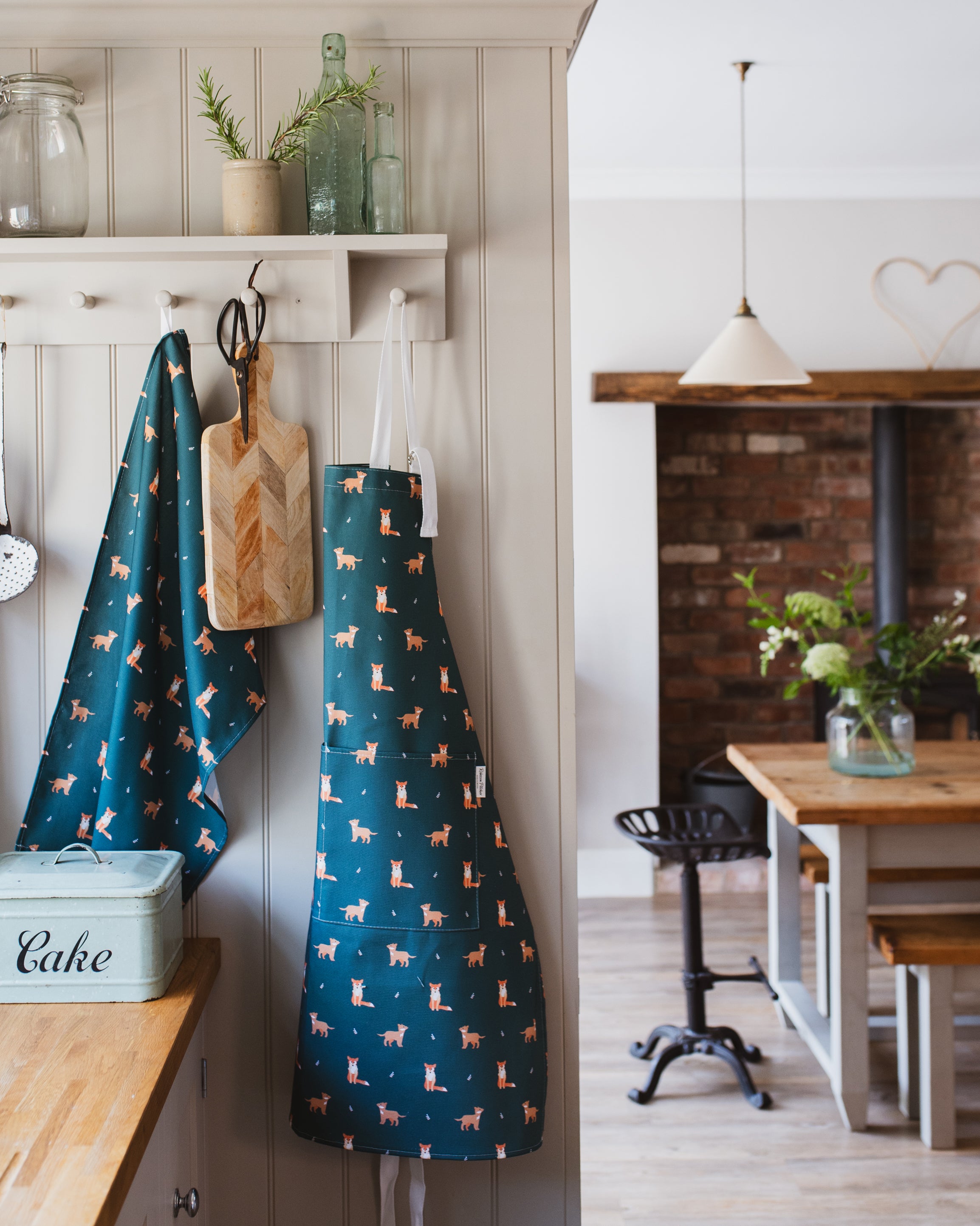 Dark Green apron with fox pattern hanging on a hook in a kitchen.