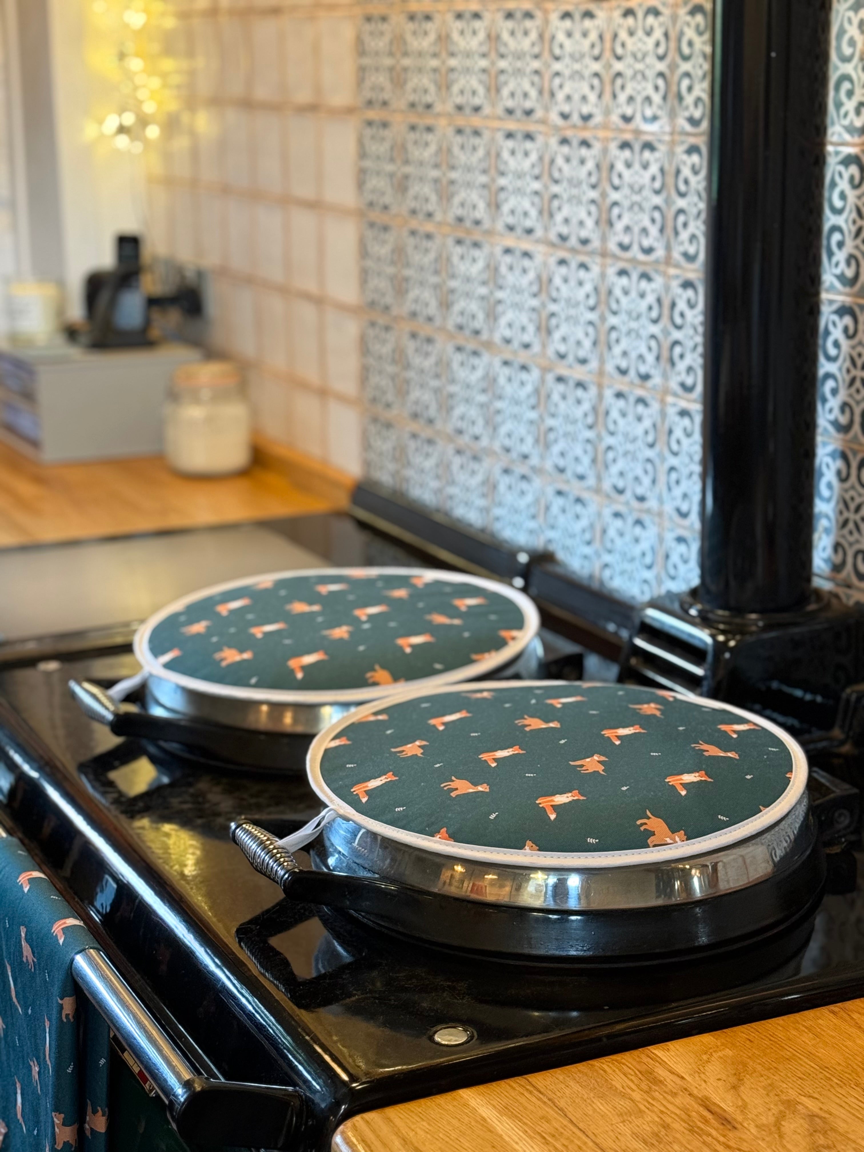 Two round green hob covers with fox pattern on a stove in a kitchen.
