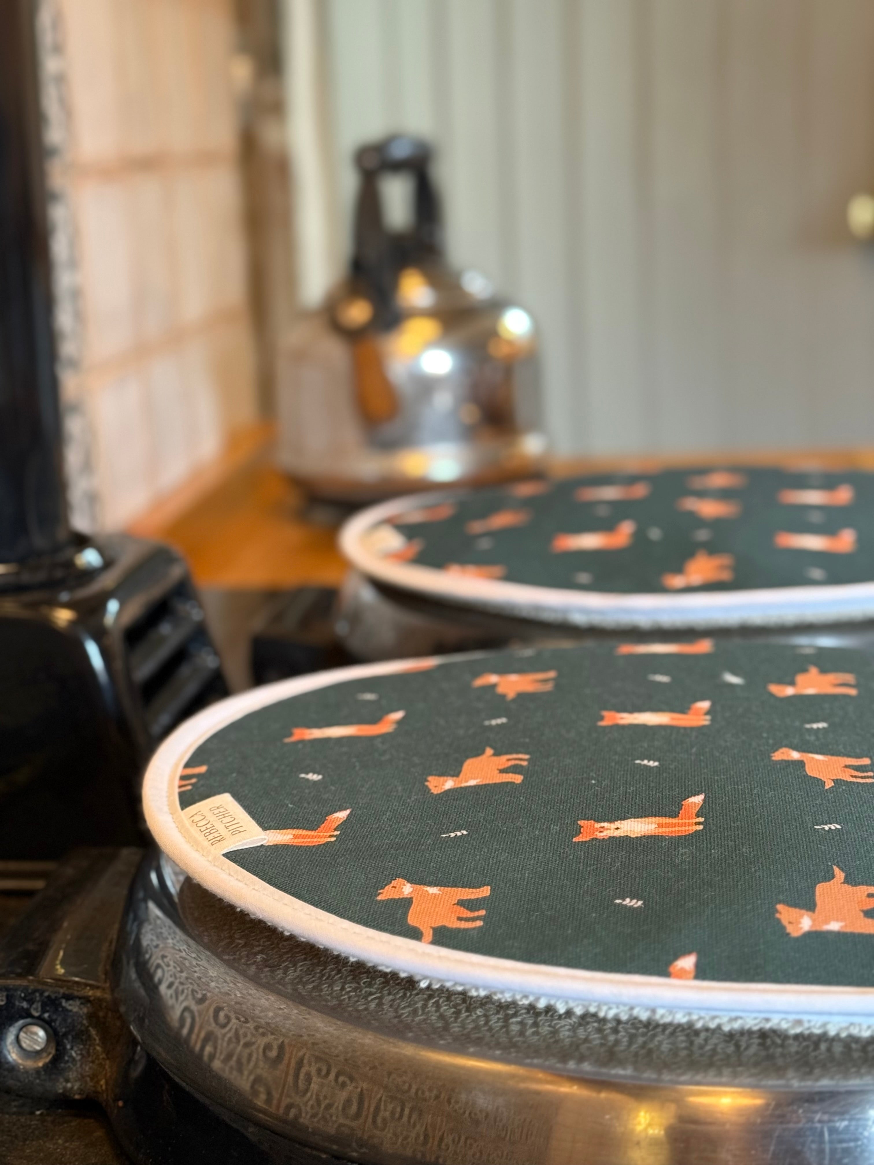 Two round green hob covers with orange fox pattern on a stove