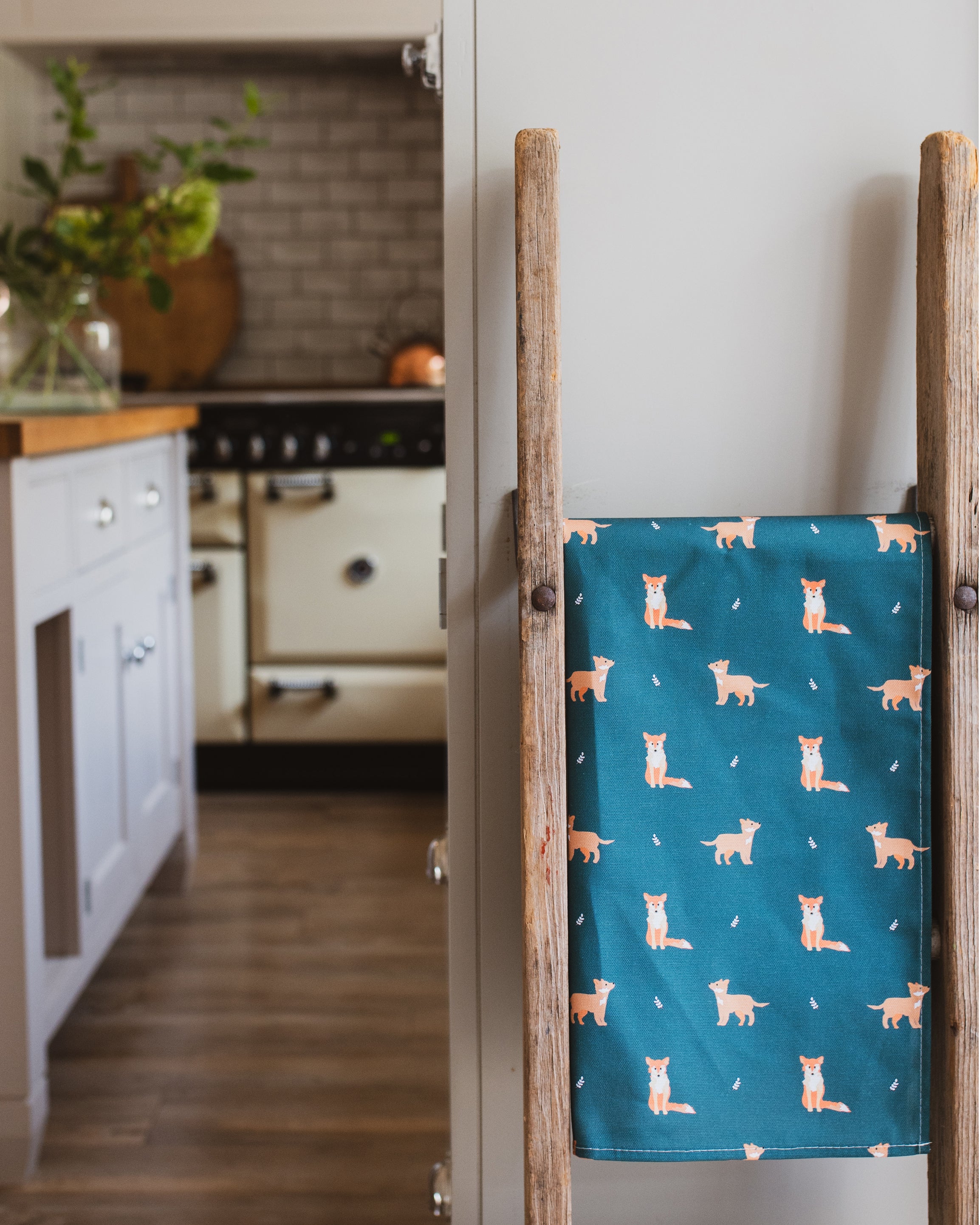 Dark Green tea towel with fox pattern hanging on a wooden rack in a kitchen.
