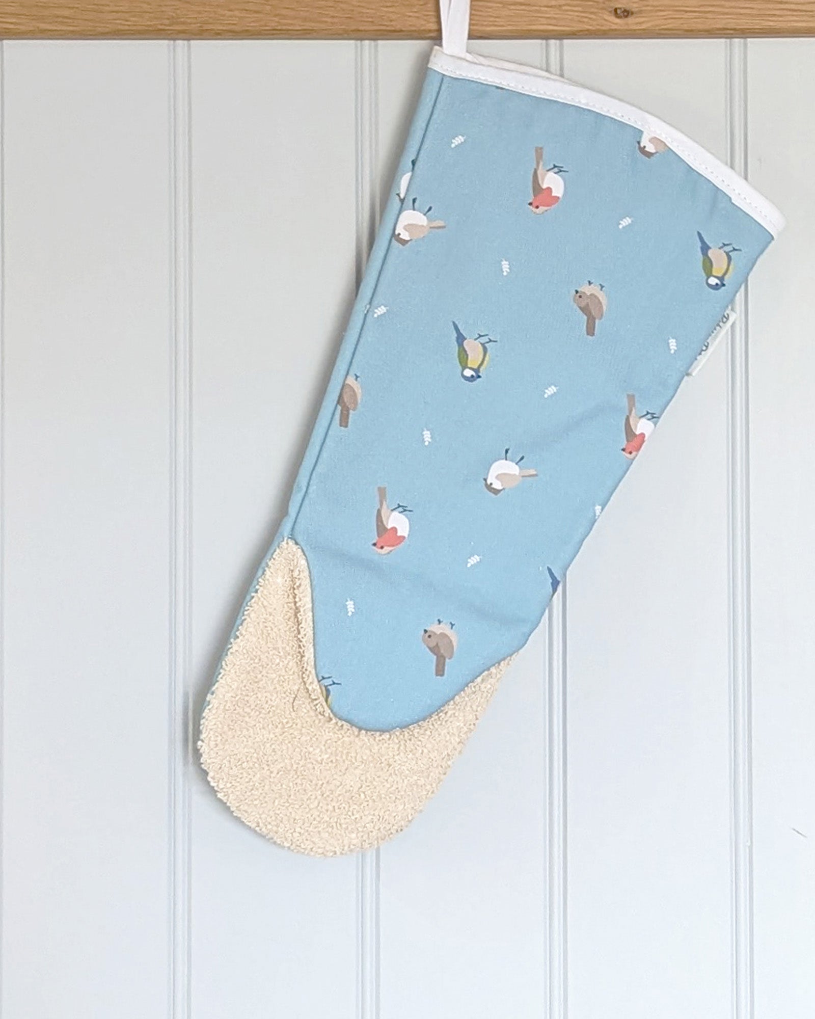 Ocean Blue Long oven gauntlet with bird patterns hanging on a white wooden background