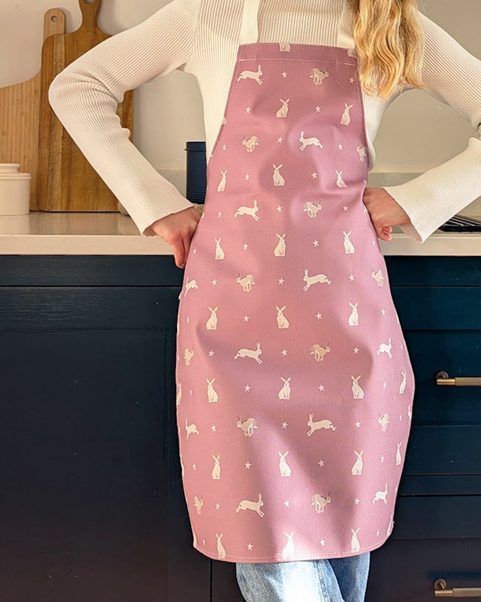Child wearing a pink apron with hare patterns in a kitchen setting
